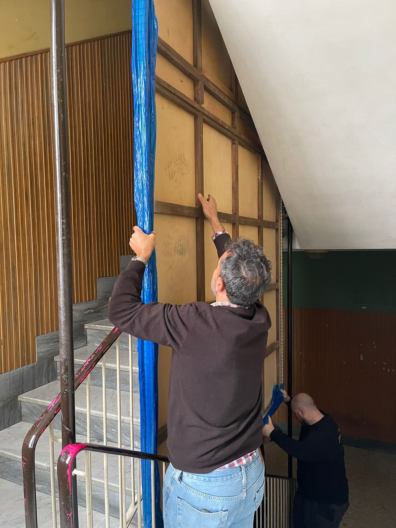 Due persone installano una struttura a muro e dell'isolamento blu in una stanza interna non rifinita.
