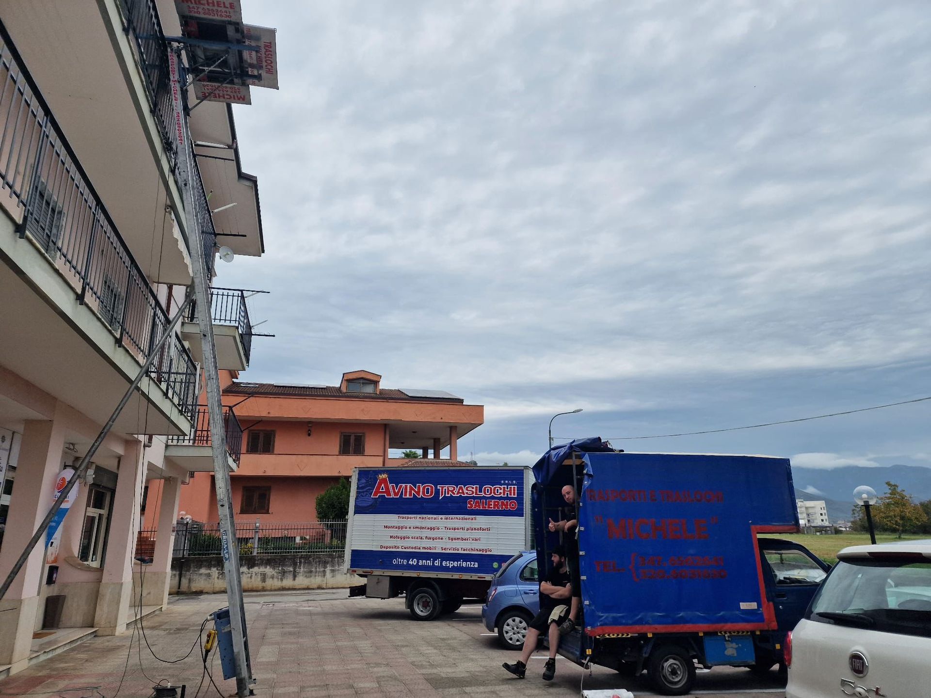 Un camioncino blu per le consegne parcheggiato in una strada accanto ad alcuni edifici, sotto un cielo nuvoloso.