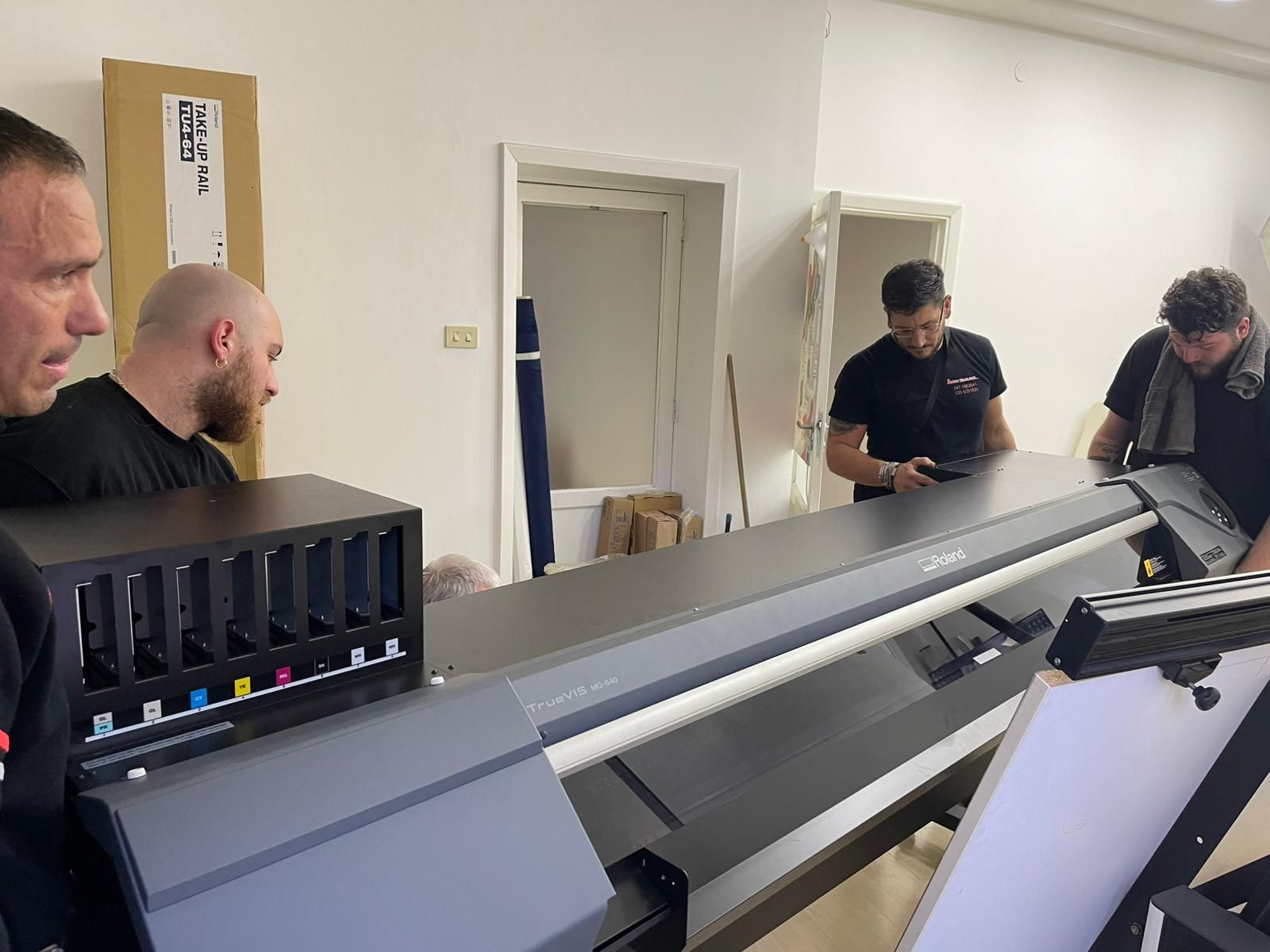 Persone che ispezionano una grande stampante in un'officina, con i pannelli aperti e gli attrezzi nelle vicinanze.