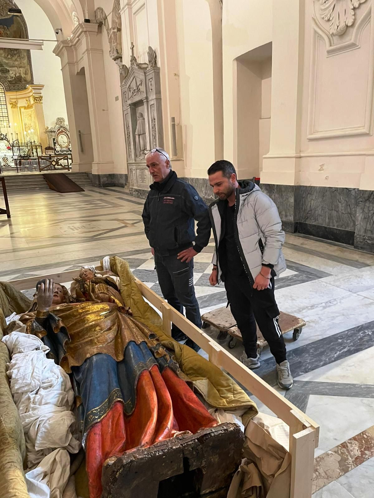 Due uomini sono in piedi accanto a una tomba riccamente decorata e dorata all'interno di una grande chiesa.