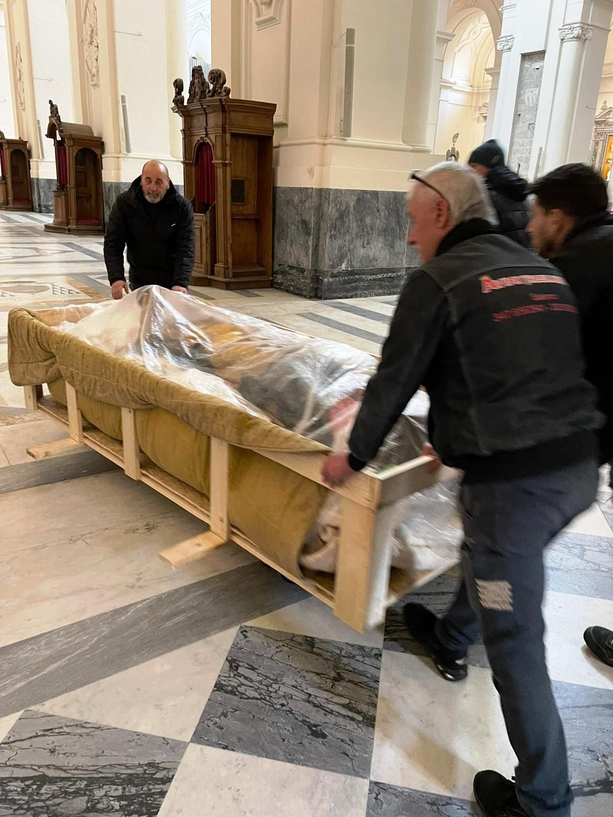 Diversi uomini spingono una grande cassa di legno imballata attraverso la navata di una chiesa.