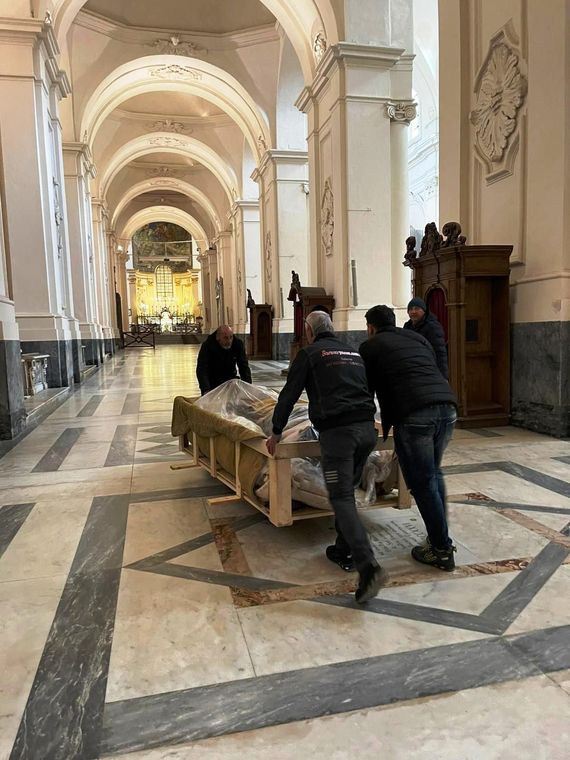Due persone spingono una lunga panca di legno attraverso la navata di una grande chiesa.