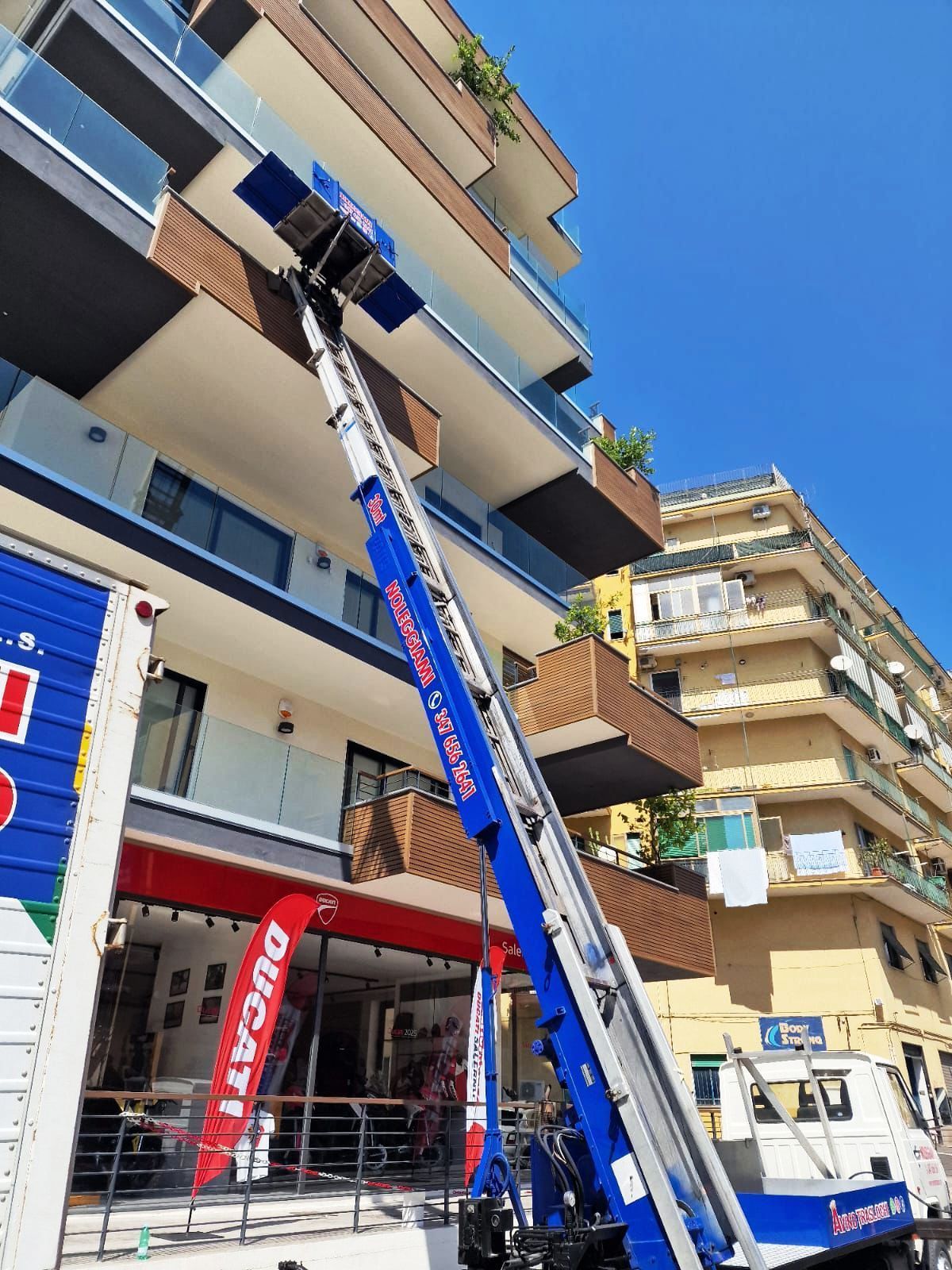 Una piattaforma elevatrice blu raggiunge i piani superiori di un edificio adiacente al marciapiede.