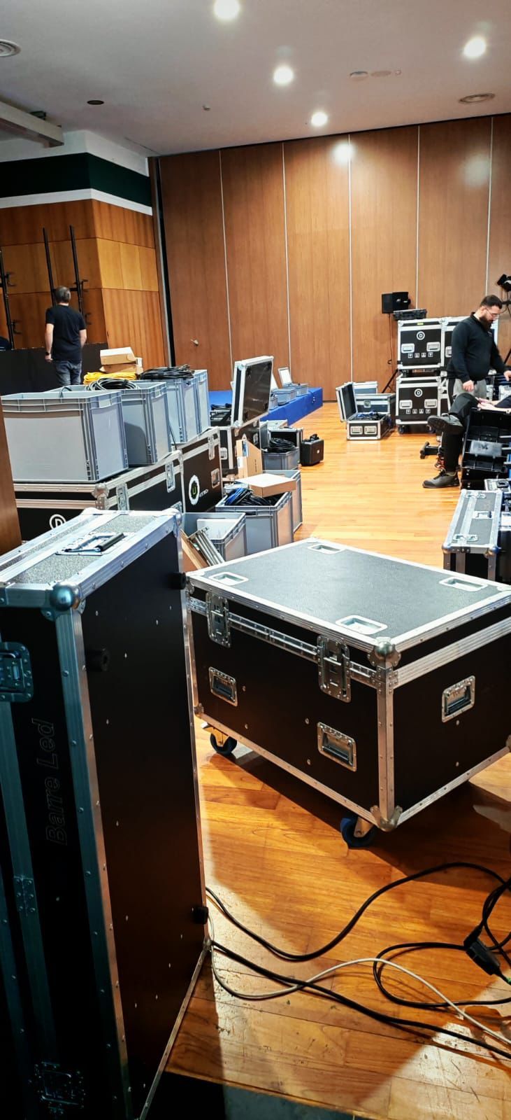 Sala di controllo dello studio con apparecchiature audio, custodie rigide nere, cavi e una persona seduta a una postazione di lavoro.