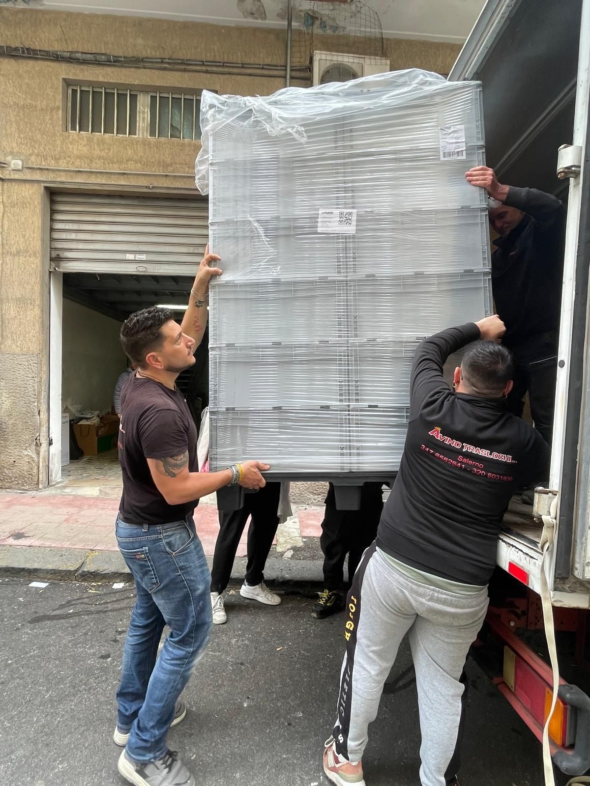 Operai caricano un grande pallet avvolto nella plastica su un camion in un vicolo.