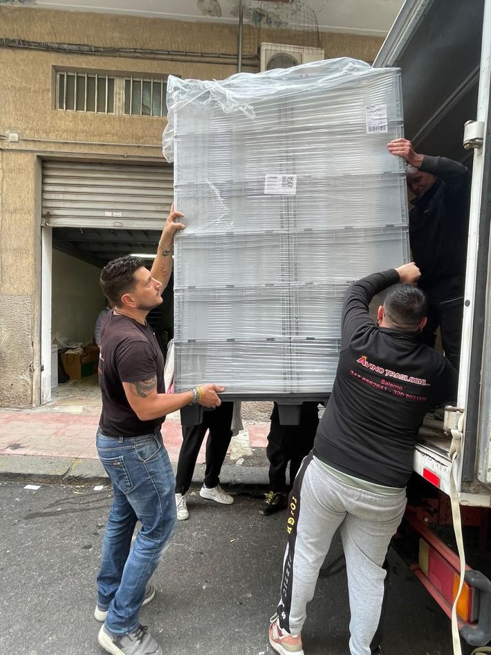 Operai caricano un grande pallet avvolto nella plastica su un camion in un vicolo.