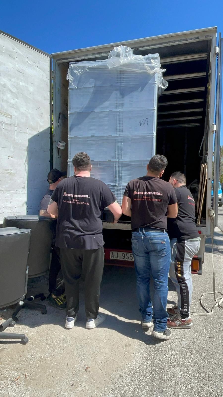 Tre operai scaricano un grande pallet imballato da un camion nell'area di carico di un magazzino.