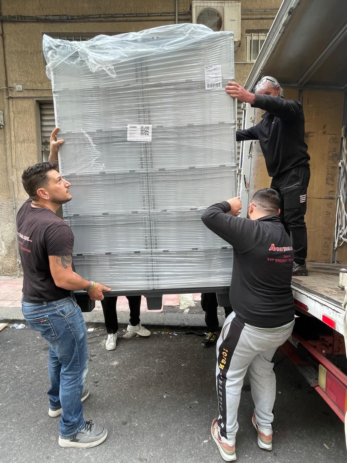 Operai che caricano un grande pallet avvolto su un camion all'esterno di un edificio.