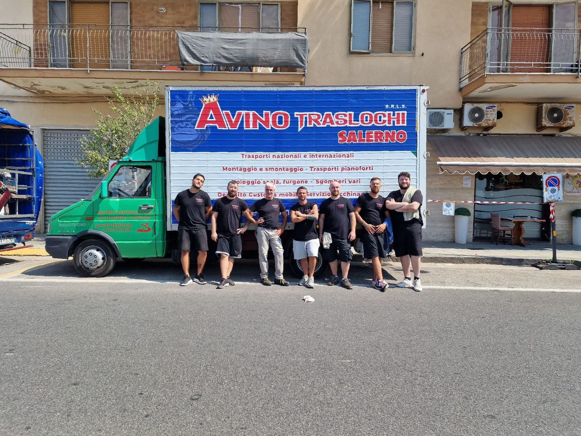 Gruppo in posa davanti a un camion verde con l'insegna blu e rossa della ditta di traslochi