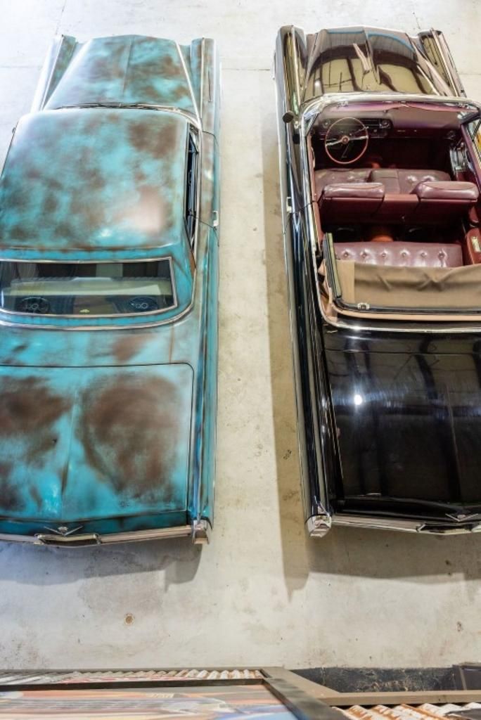 Two old cars are parked next to each other in a garage.
