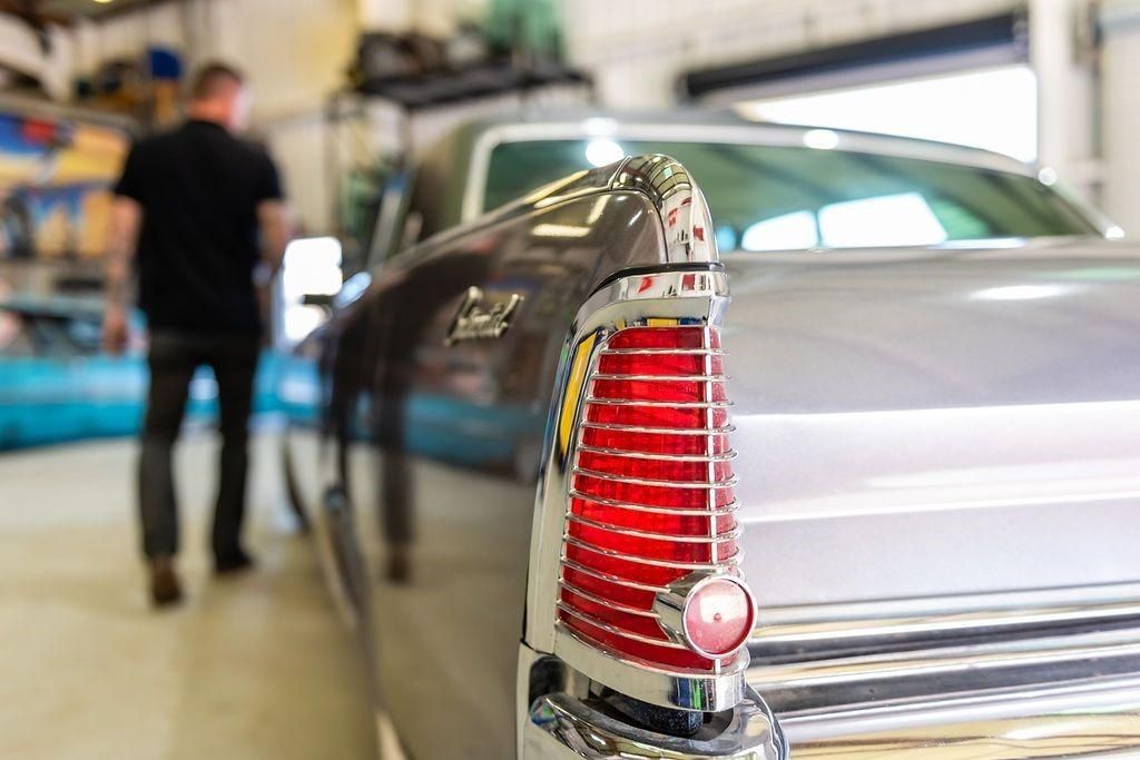 A man is standing in front of a car in a garage.