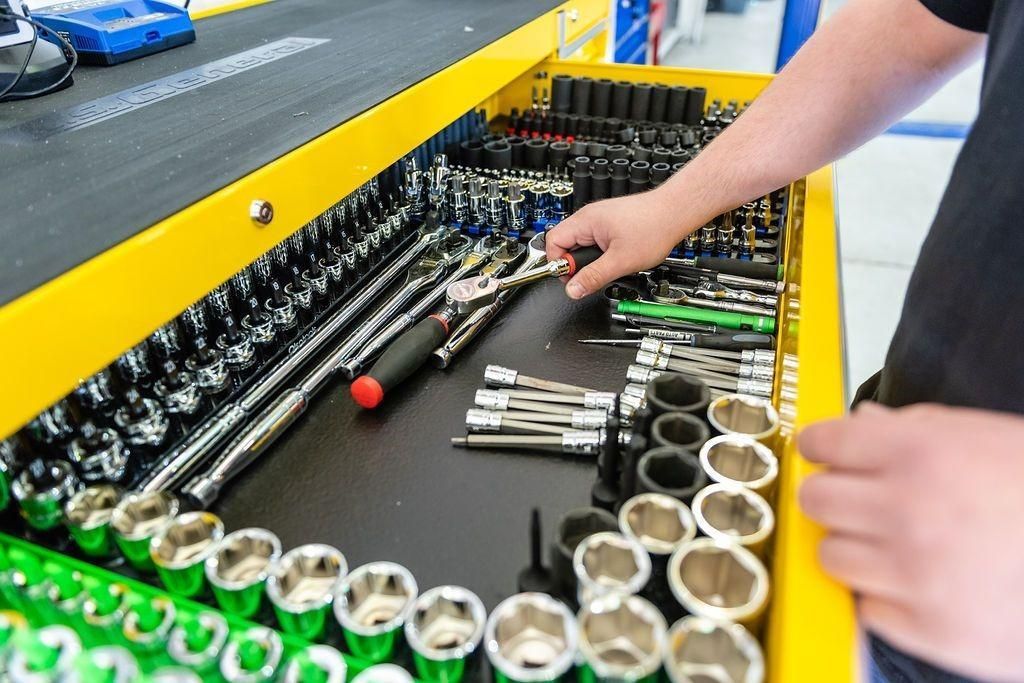 A person is reaching for a wrench in a toolbox filled with tools.