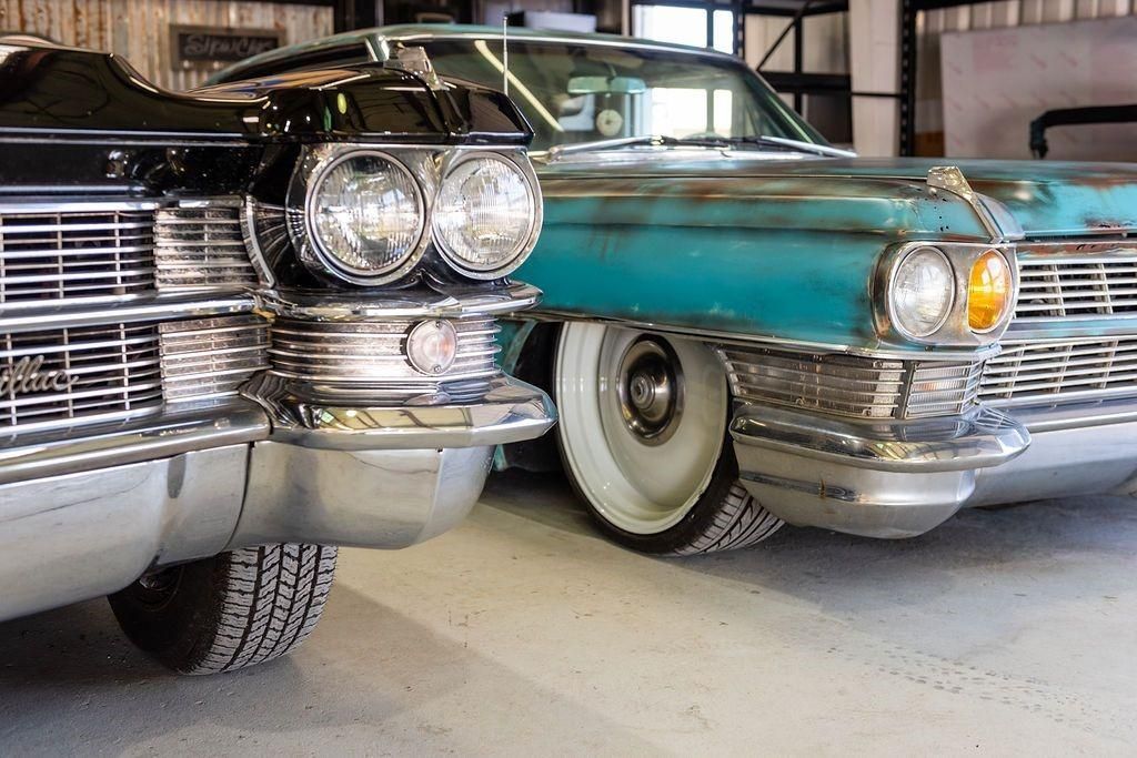 Two old cars are parked next to each other in a garage.