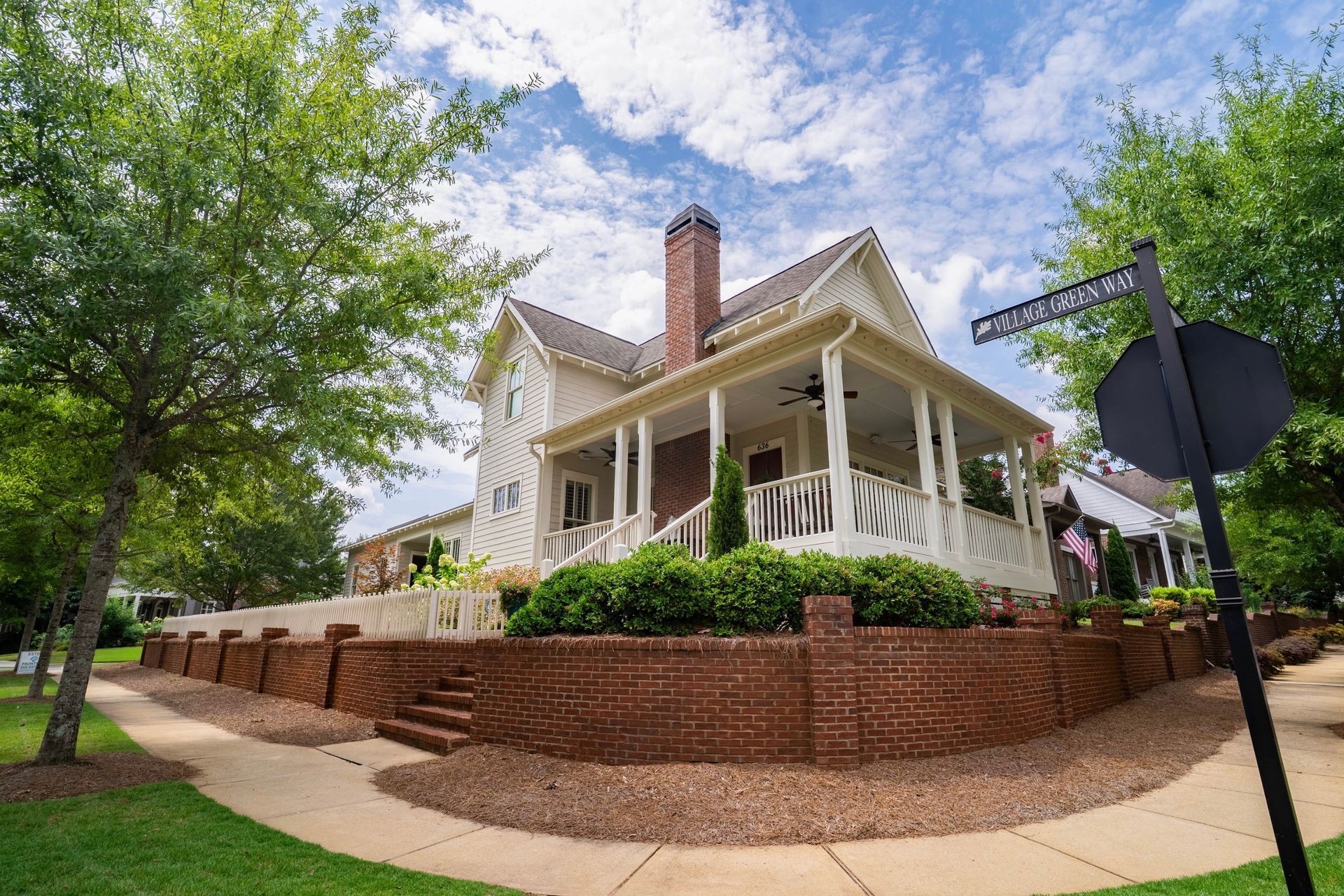 White house with porch on a brick terrace, surrounded by green trees under a blue sky