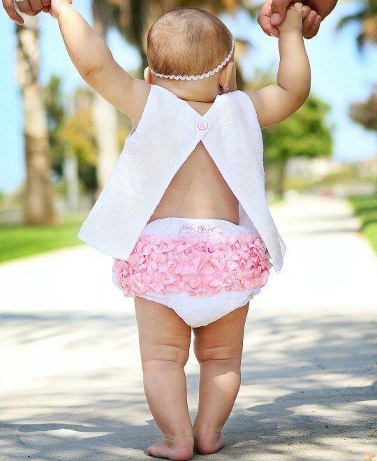 A baby wearing a diaper and a white top is being held by a person