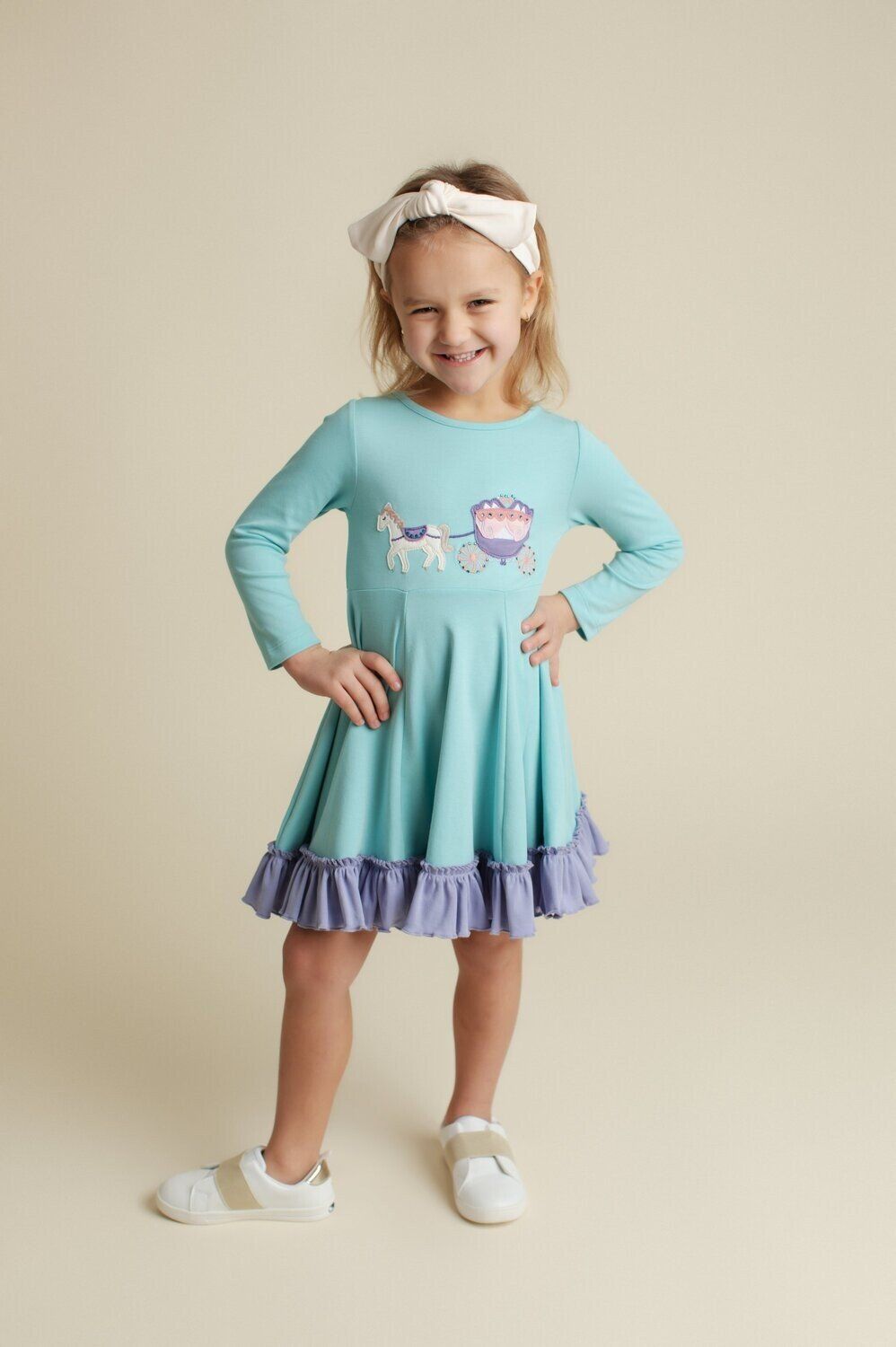 A little girl in a blue dress is standing with her hands on her hips.