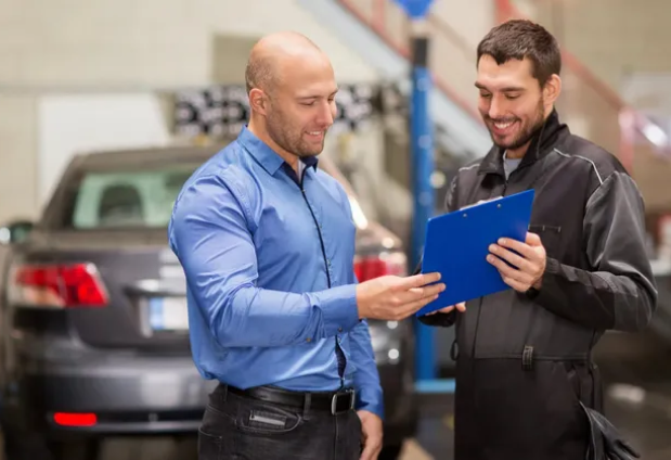 A man and mechanic reviewing paperwork in a car repair shop, both smiling.
