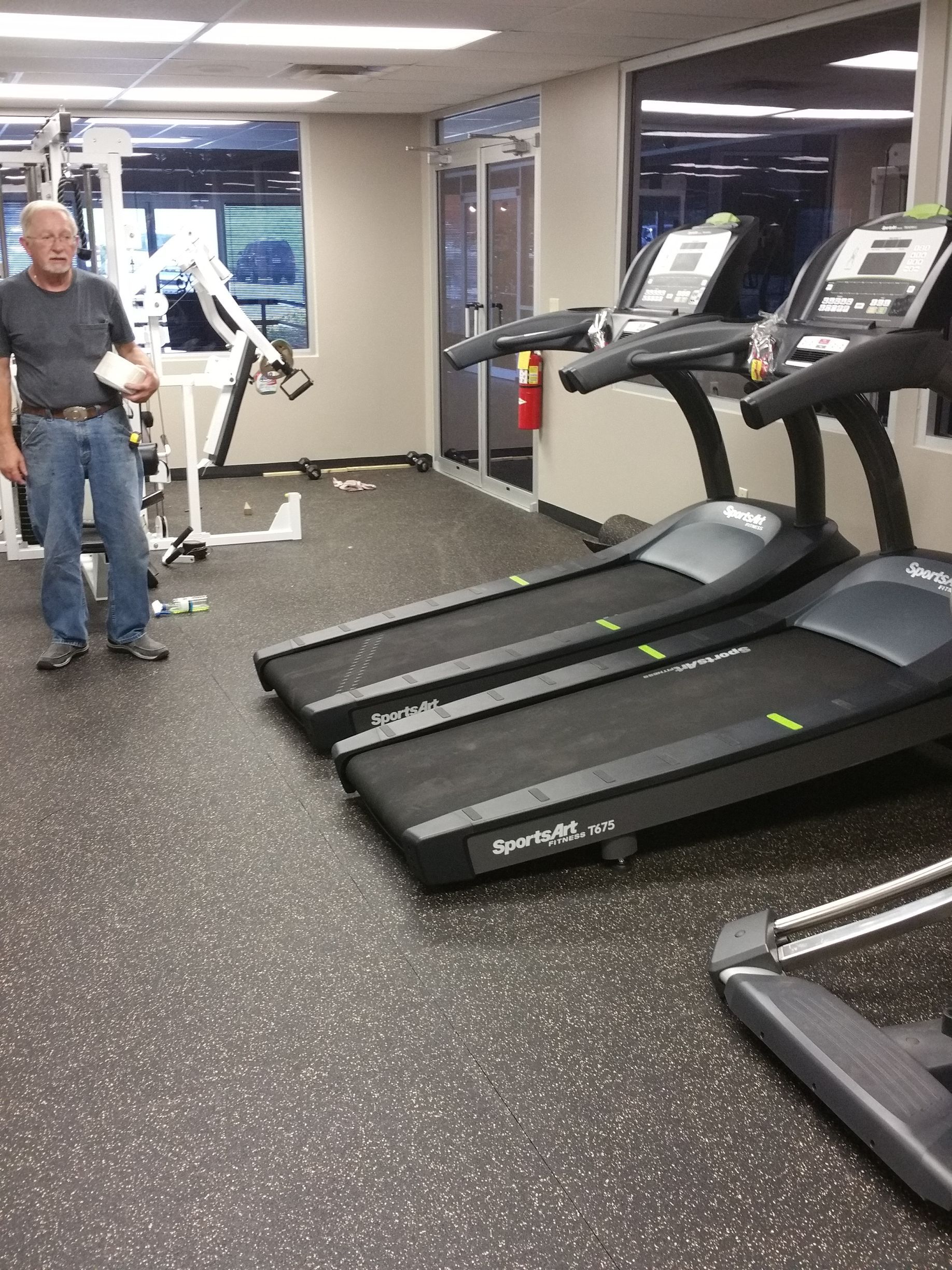 Gym with treadmills and exercise equipment; a person stands near a white machine.