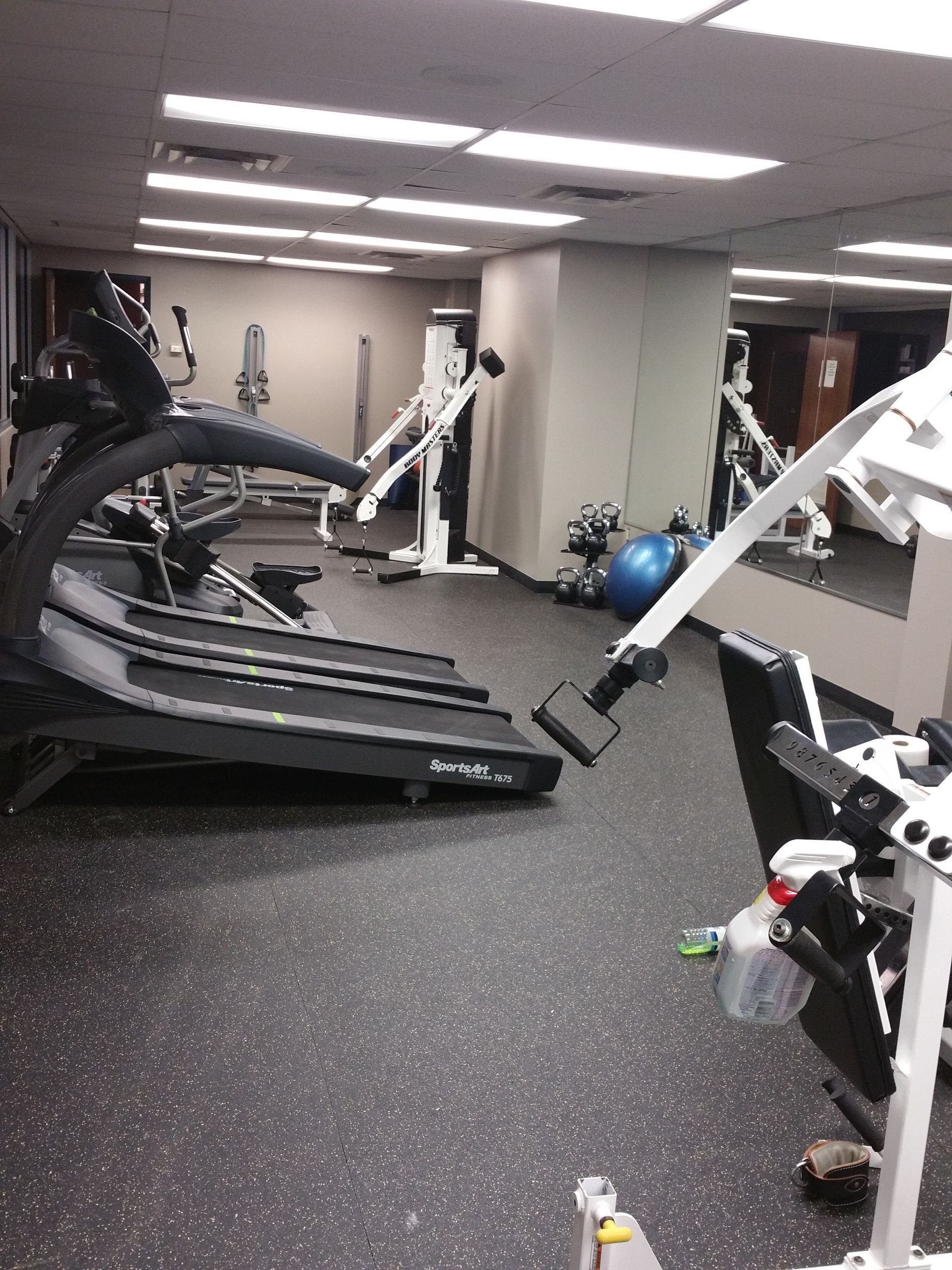 Gym with treadmills, weight machines, and a blue exercise ball under bright ceiling lights.