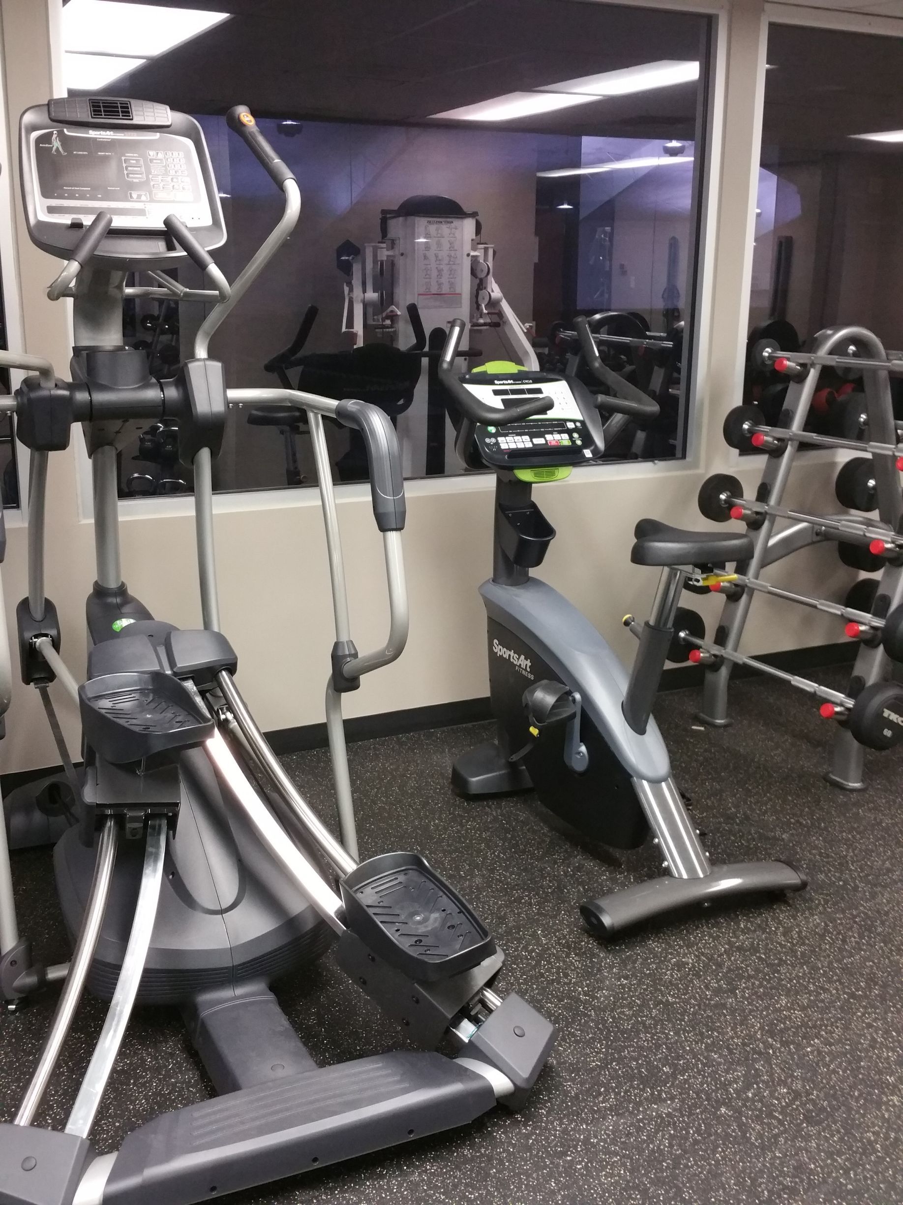 Gym with elliptical machines and a stationary bike in front of a mirrored wall.