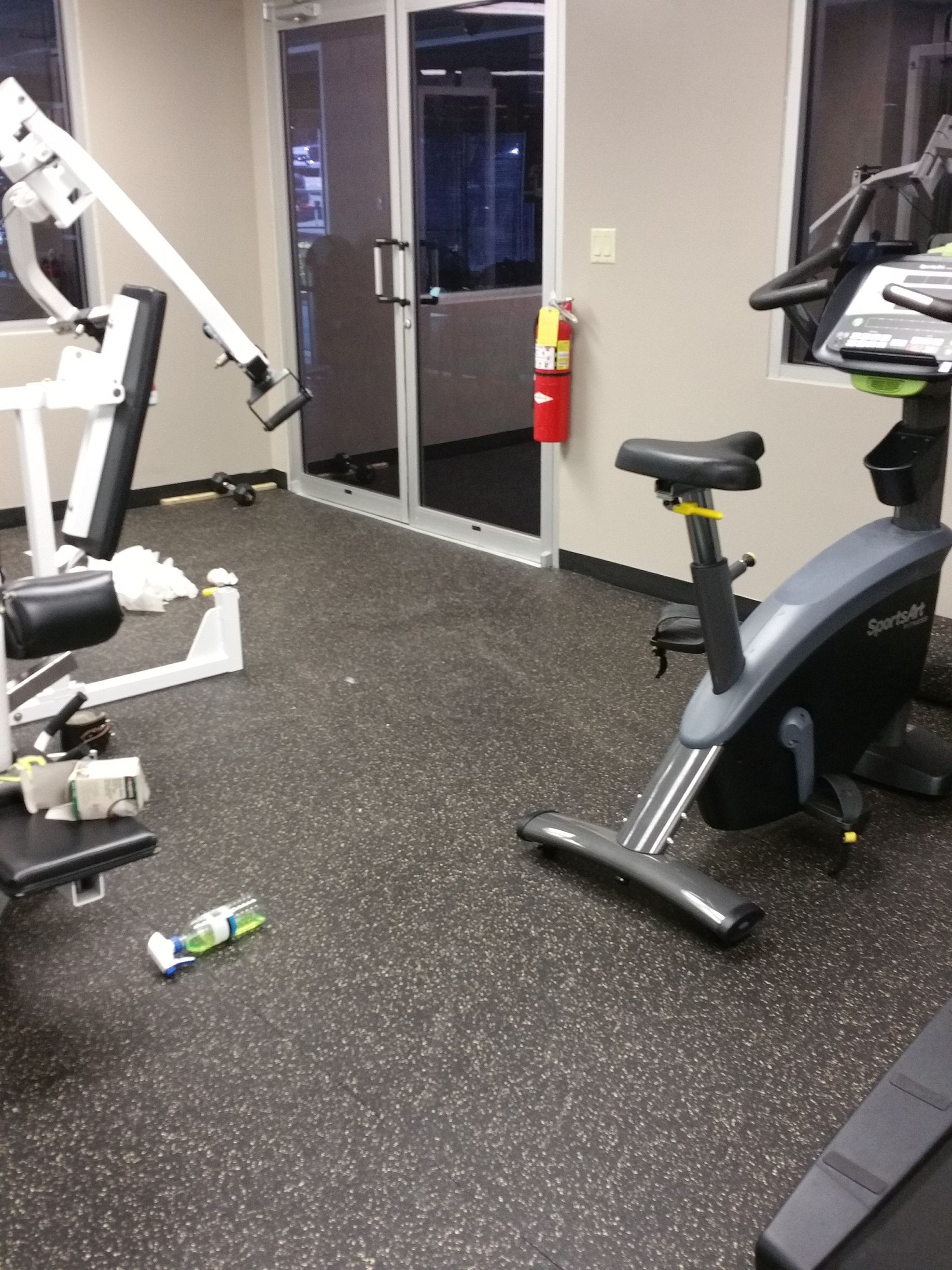 Small gym room with exercise machines, glass door, and a red fire extinguisher on the wall.