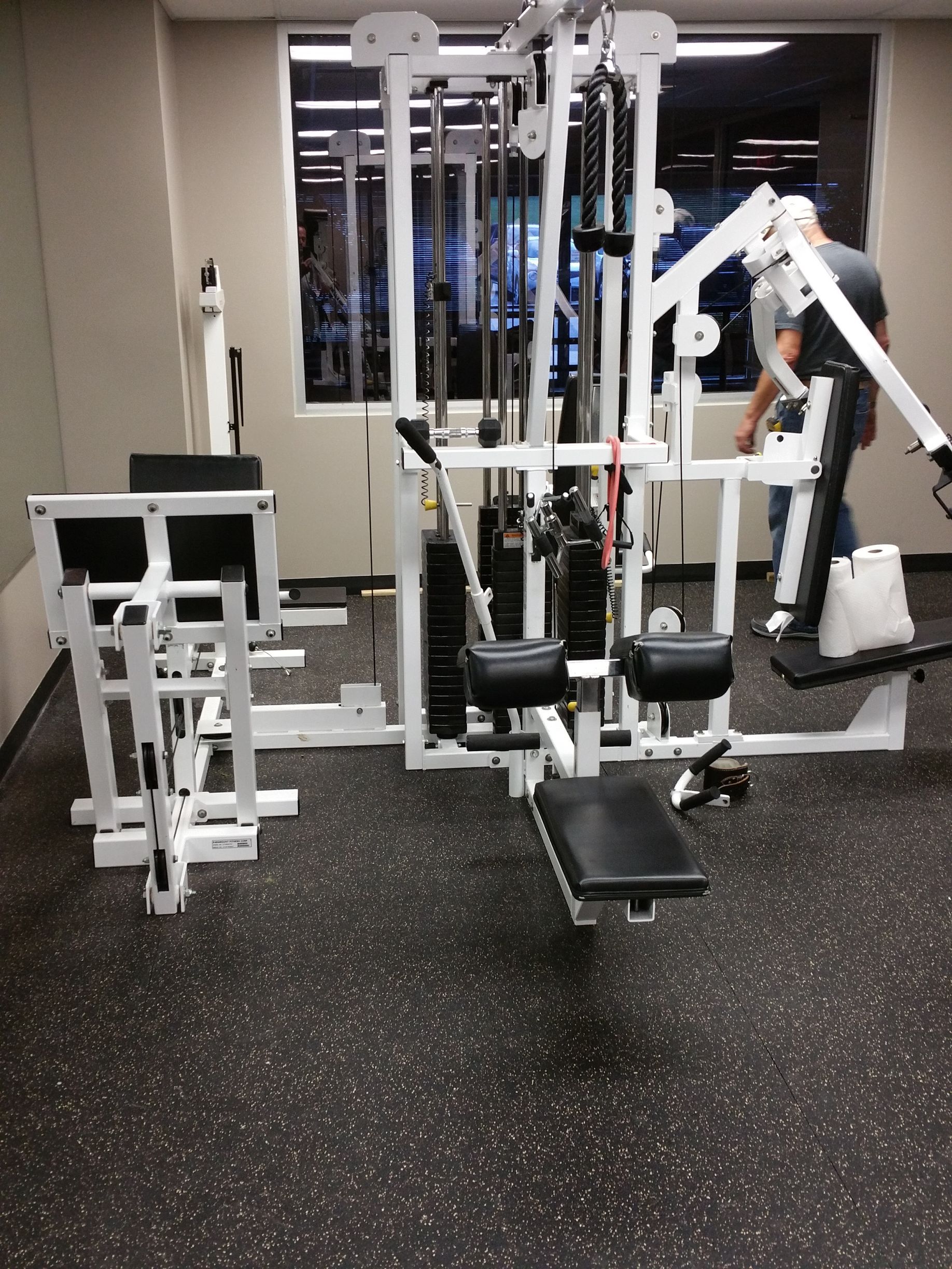 Gym machines in a fitness room with white equipment and black padded seats on speckled flooring