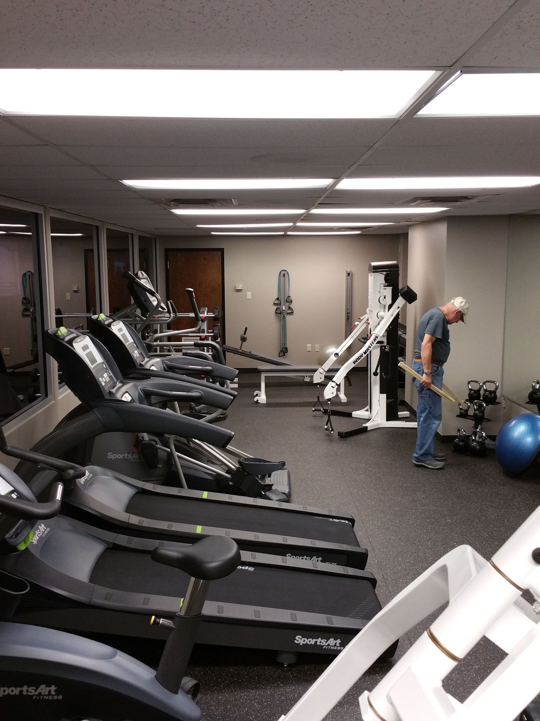 Gym interior with treadmills, weight machines, and a person standing near exercise equipment