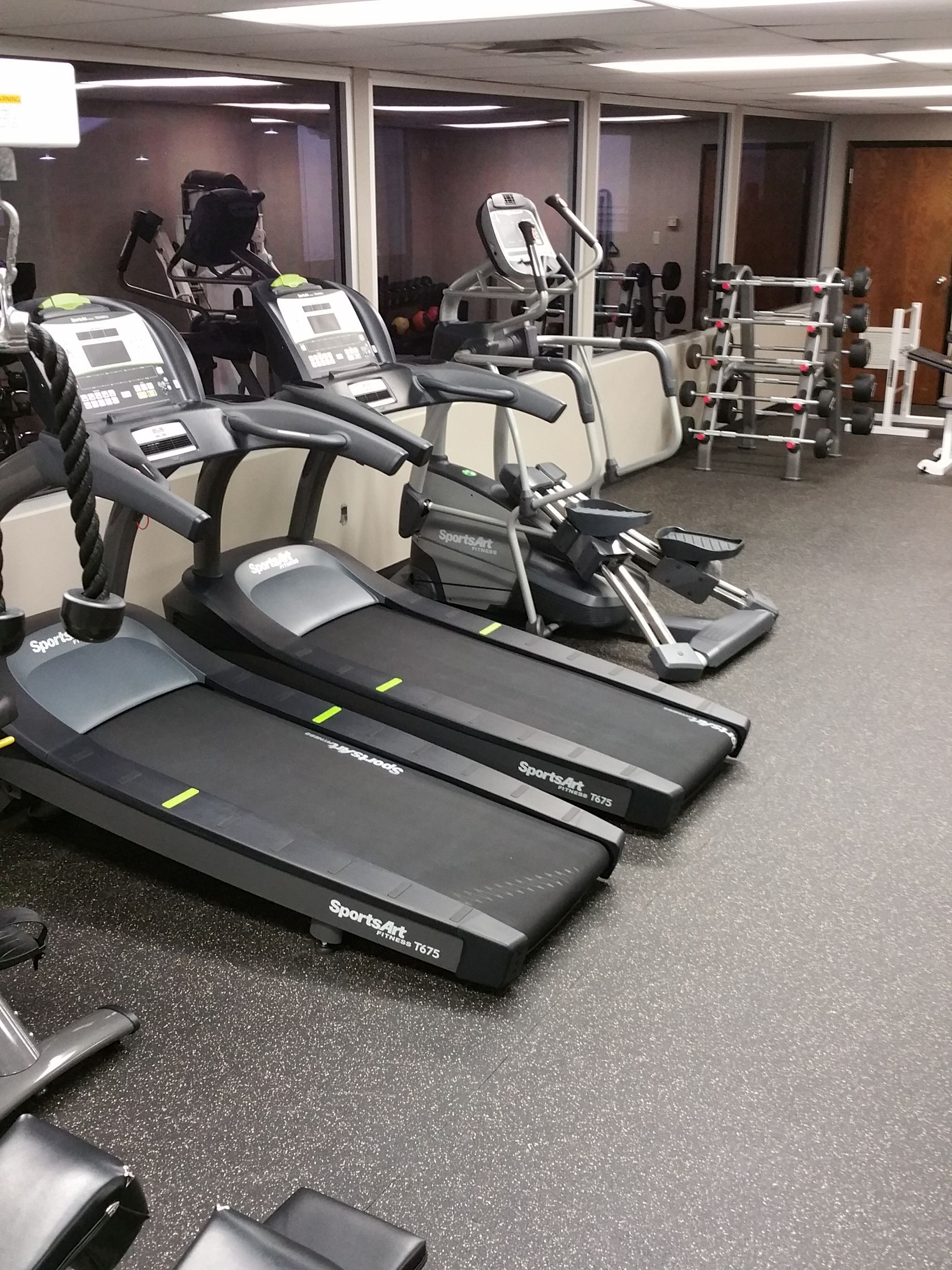 Gym room with treadmills, an elliptical, and exercise machines on rubber flooring.