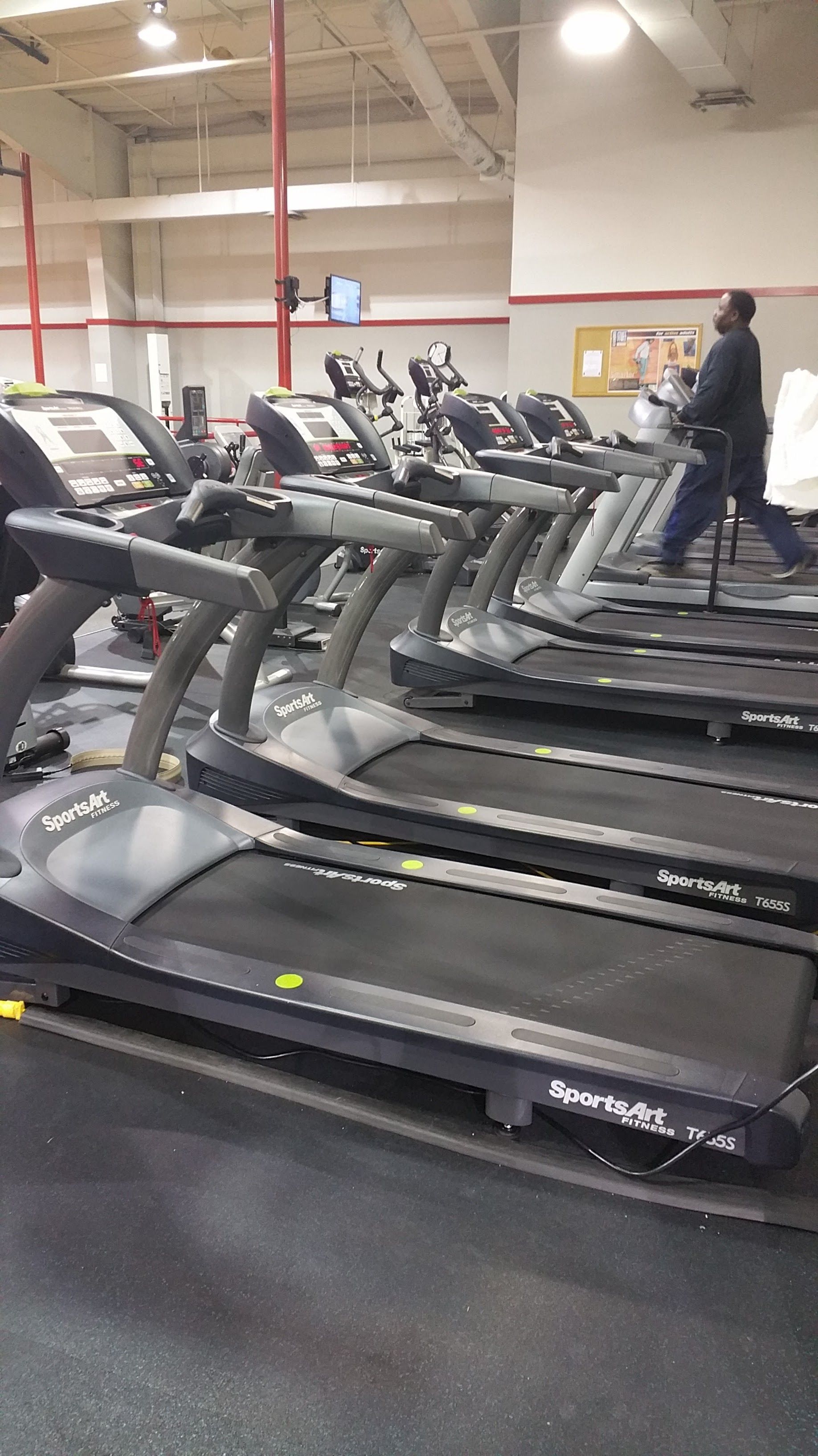 Row of treadmills in a gym, with one person exercising on the right.