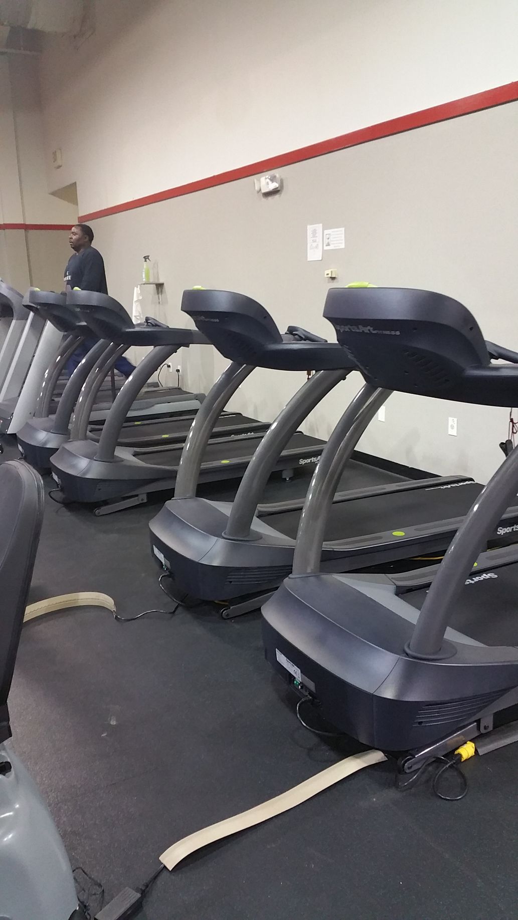 Row of treadmills in a gym, with a person standing near the back wall.