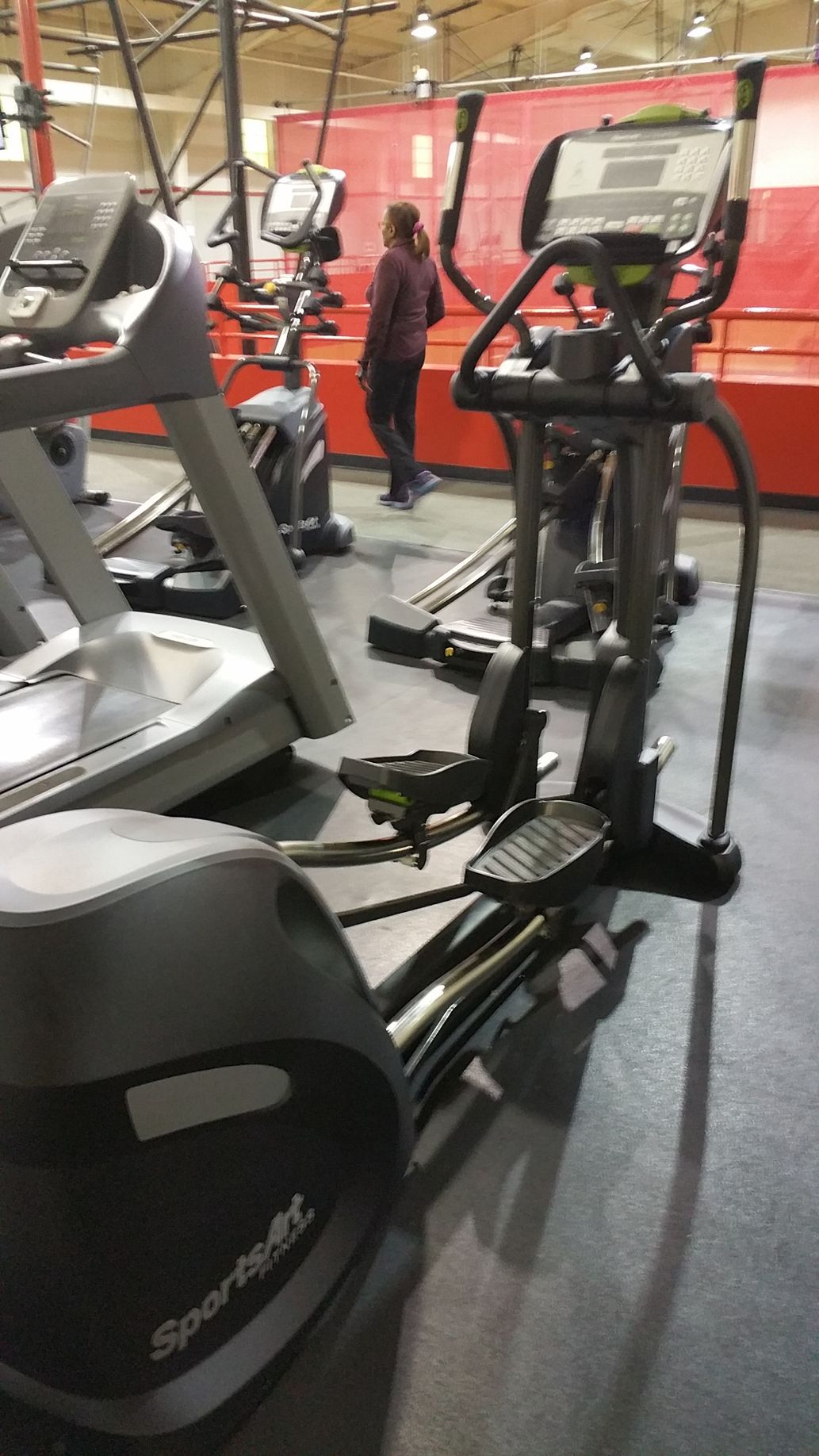 Gym with treadmills and an elliptical machine in the foreground, with people exercising in the background