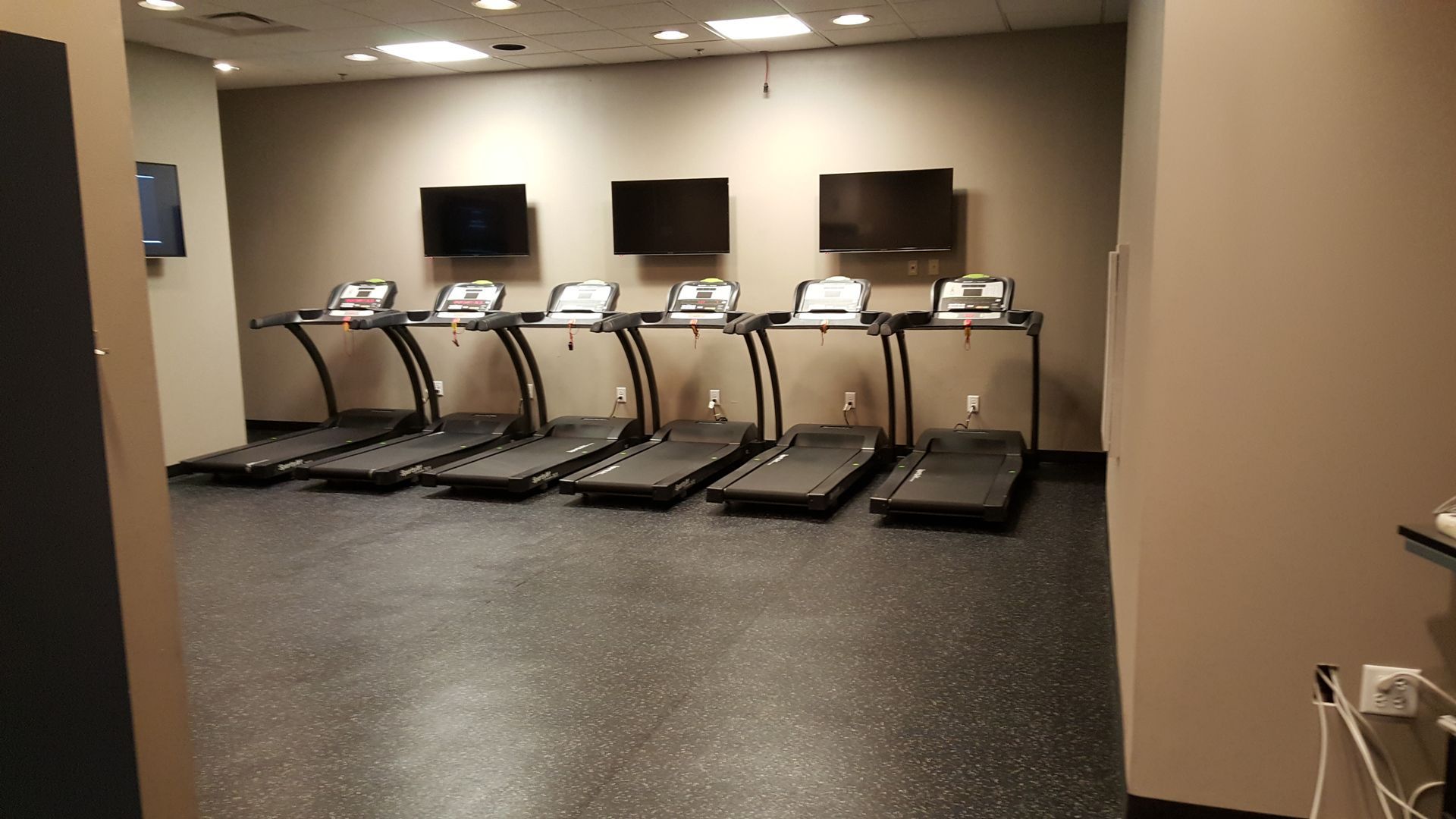 Small gym room with treadmills lined up against the wall and two wall-mounted TVs.