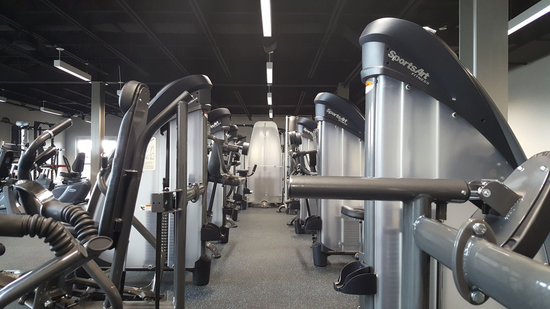 Modern gym interior with rows of weight machines and mirrors on a carpeted floor.