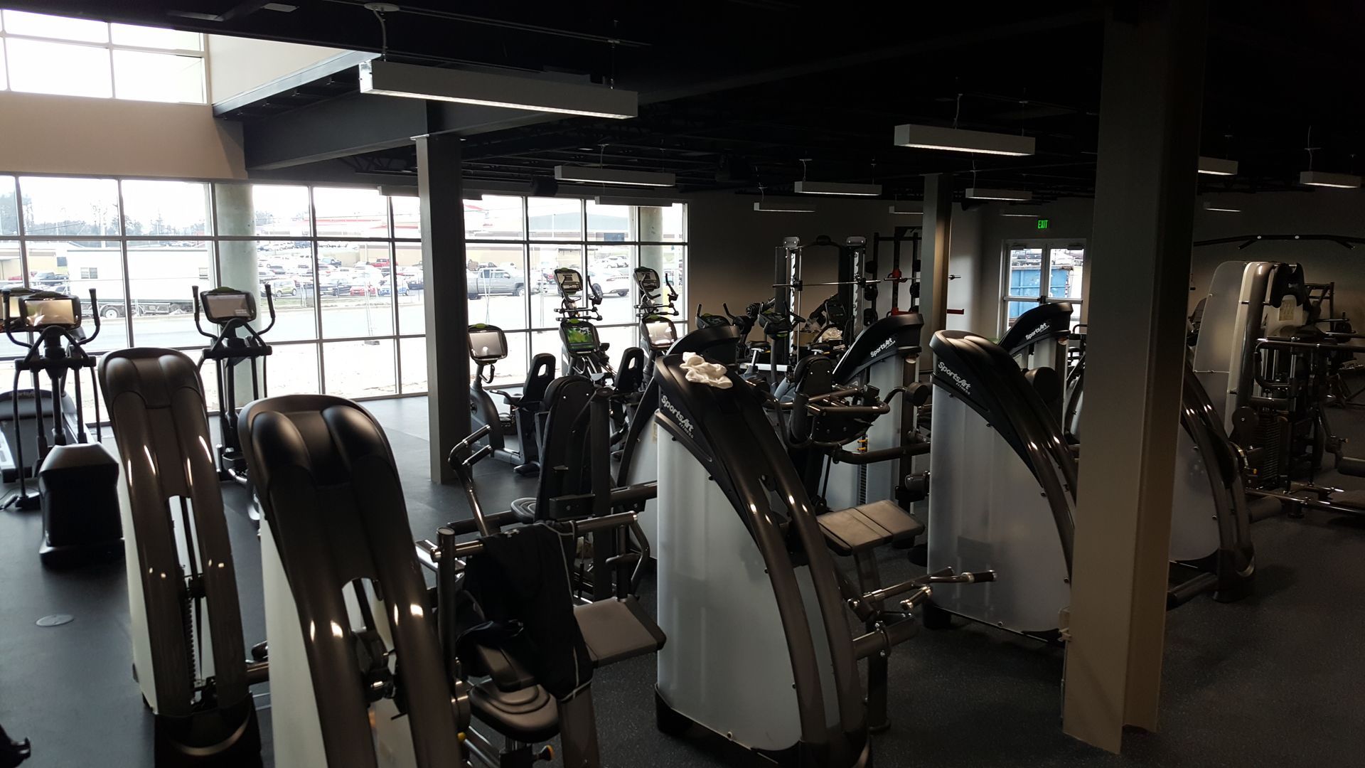 Empty gym interior with exercise machines, large windows, and mirrored walls