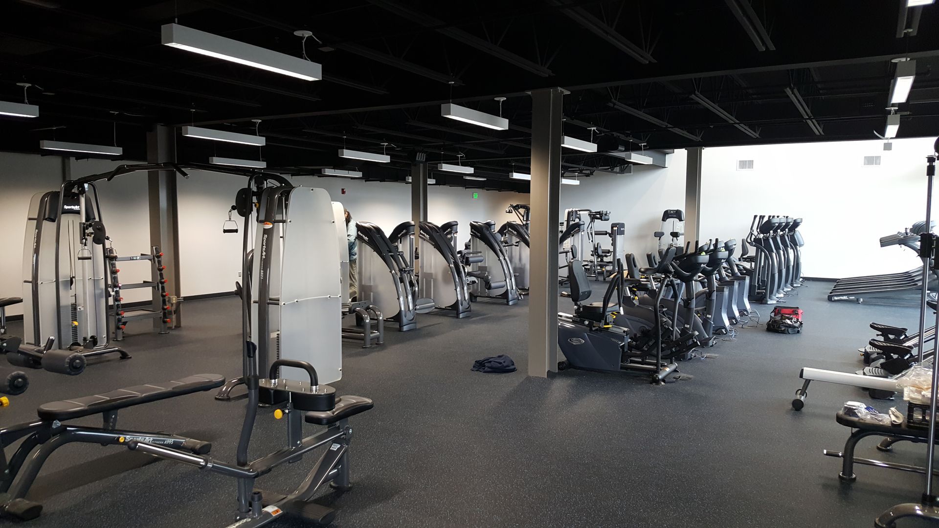 Empty gym with weight machines and benches in a dark, spacious workout room