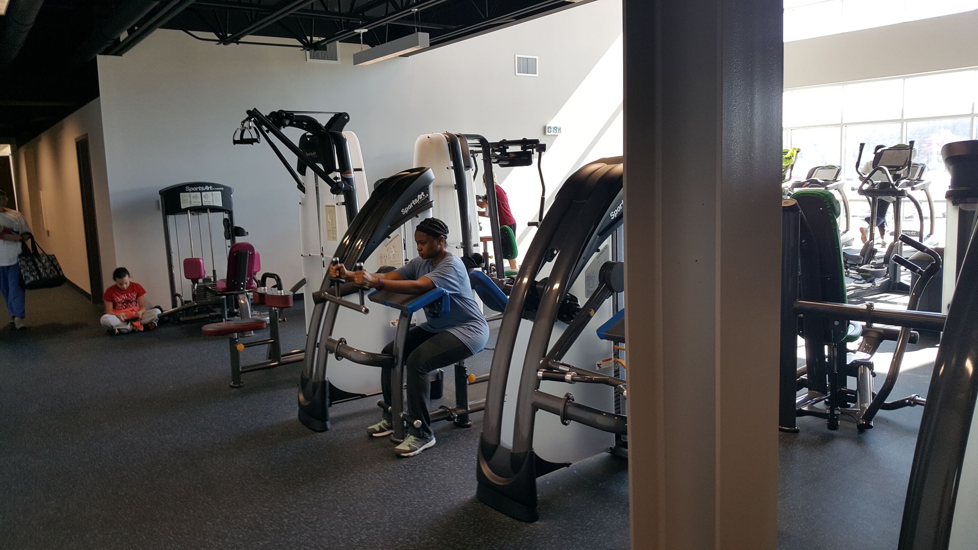 Gym with people using exercise machines and weights in a bright fitness room