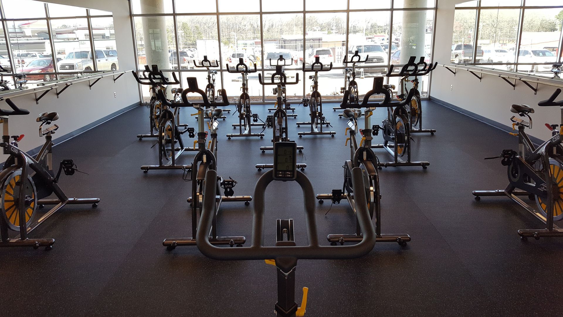 Indoor gym with rows of stationary exercise bikes and large windows in the background.