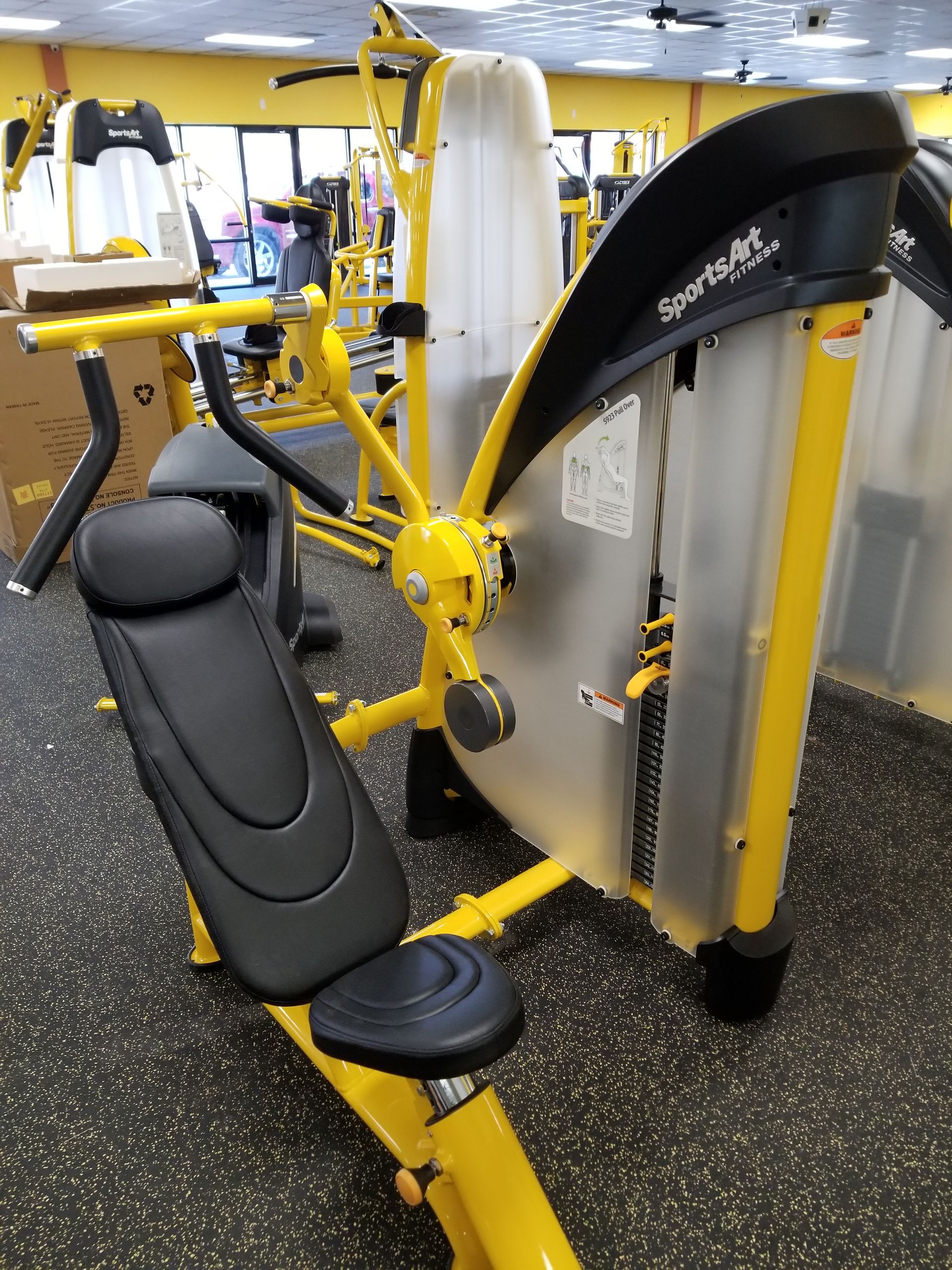 Yellow gym strength machine with black seat and padded backrest in a fitness center
