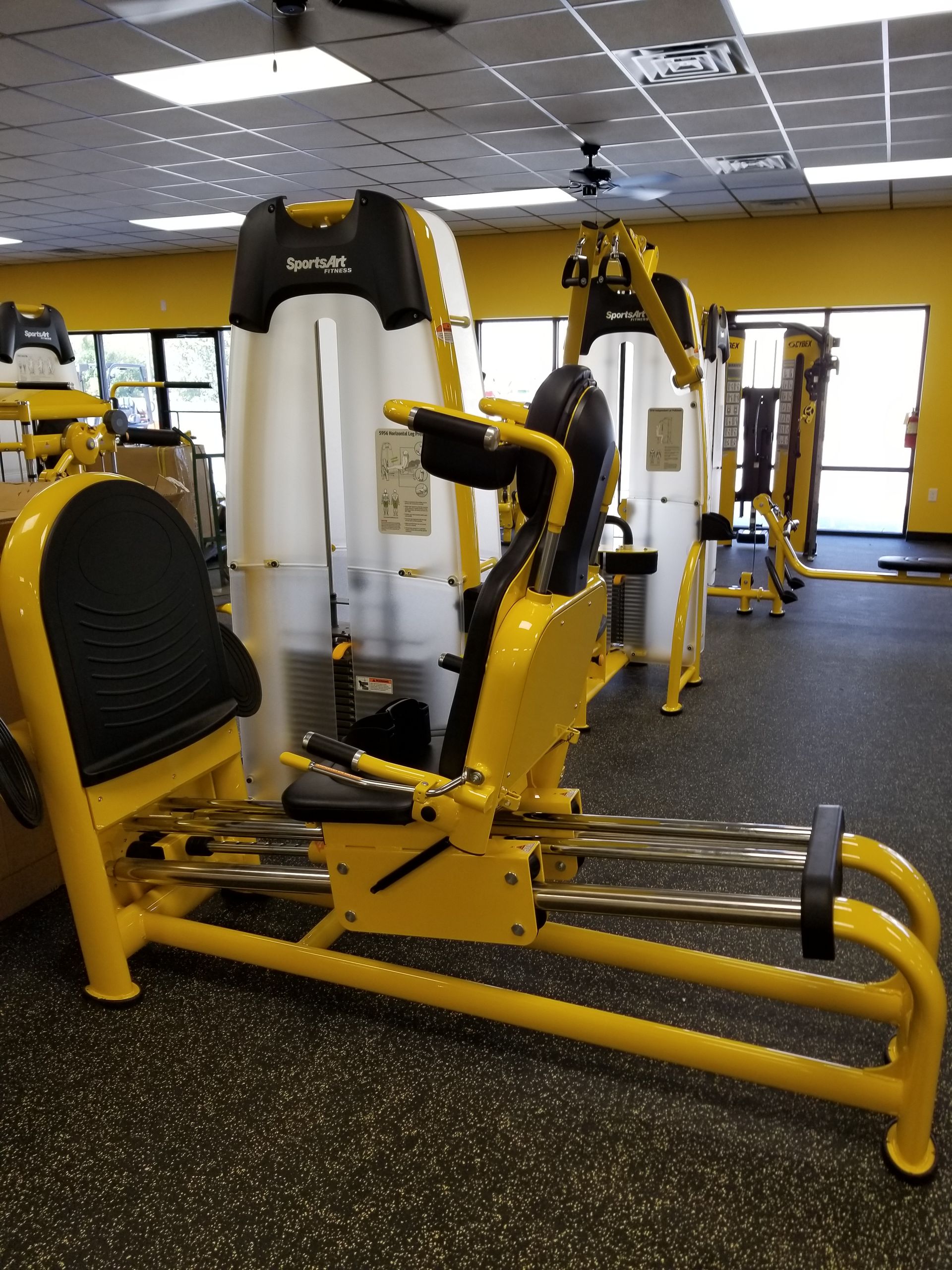 Yellow and white gym exercise machines on a black rubber floor in a fitness center