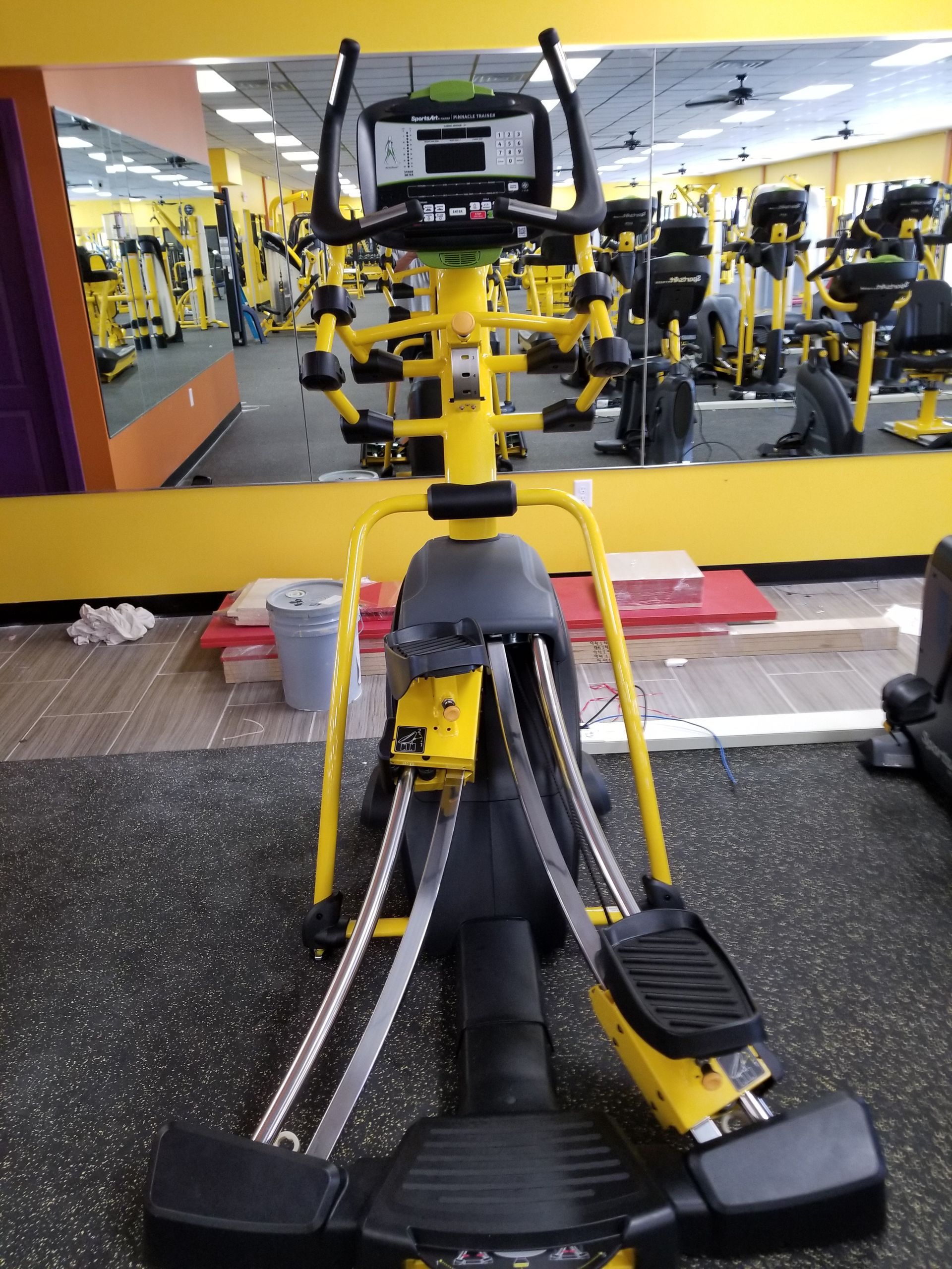 Yellow and black gym rowing machine facing a mirrored wall in a fitness center