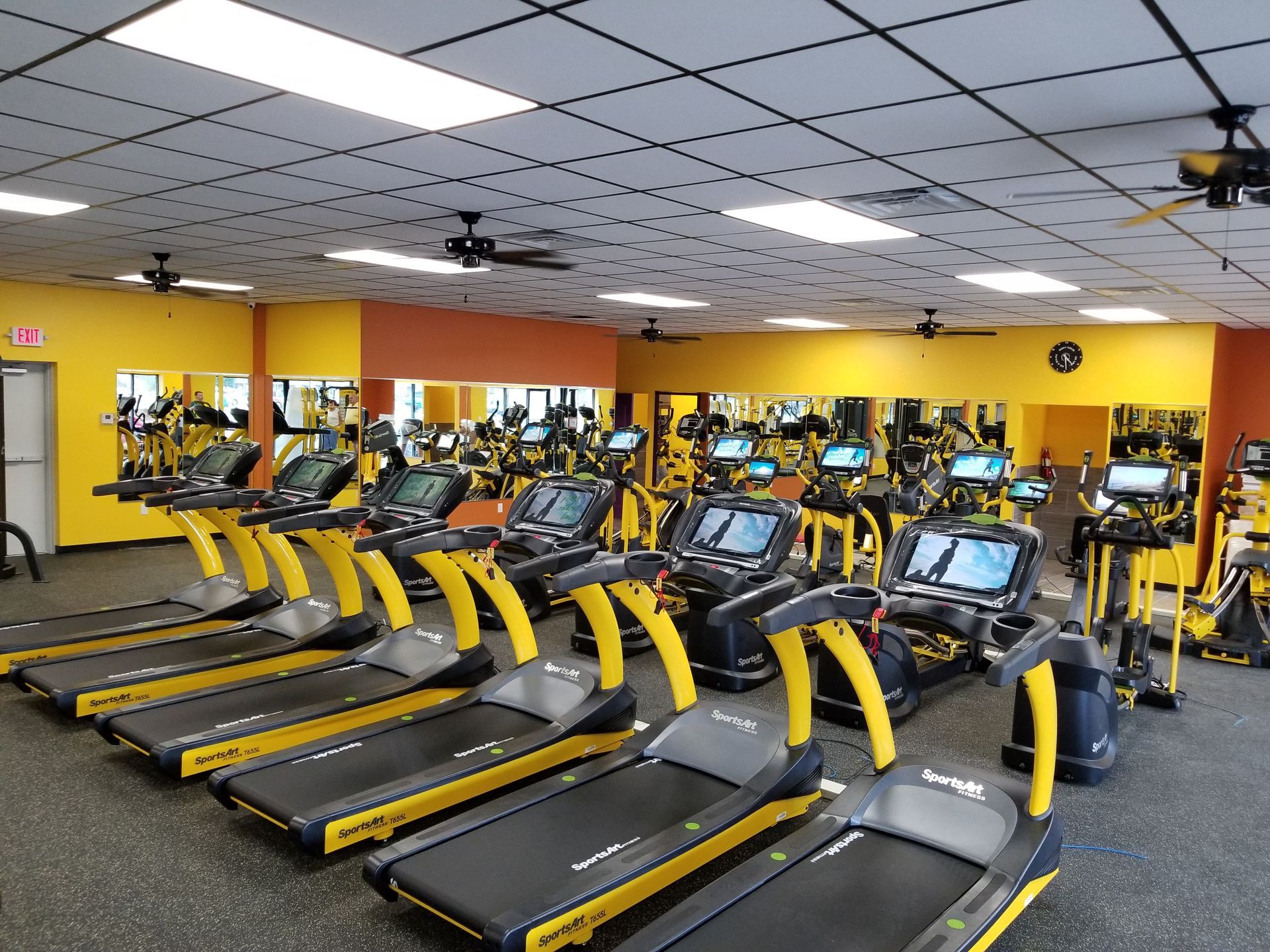 Gym with rows of black treadmills and yellow accents under bright ceiling lights