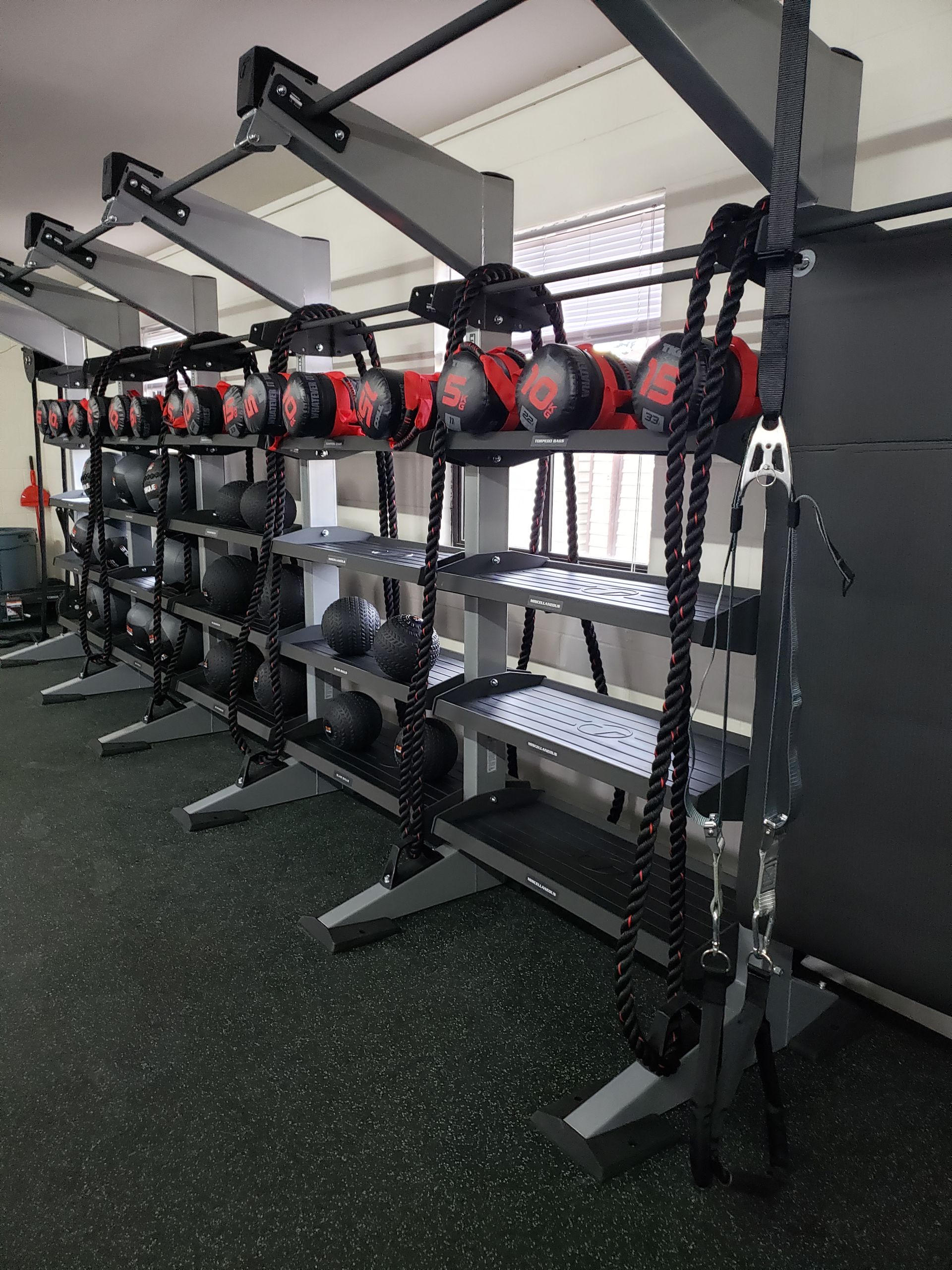 Gym rack with rows of black and red fitness belts hanging in an indoor workout area