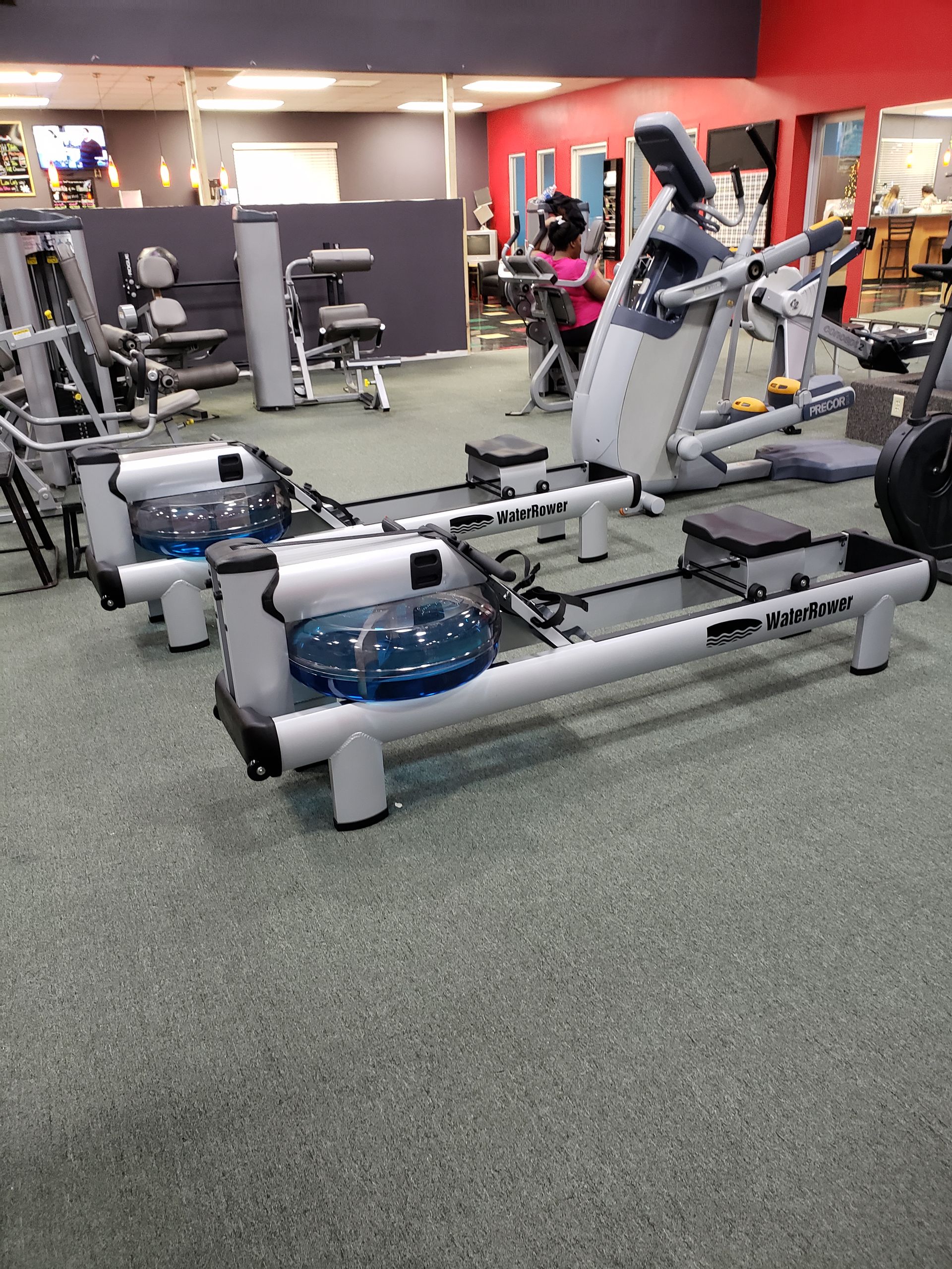 Gym interior with rowing machines and cardio equipment on a carpeted floor.