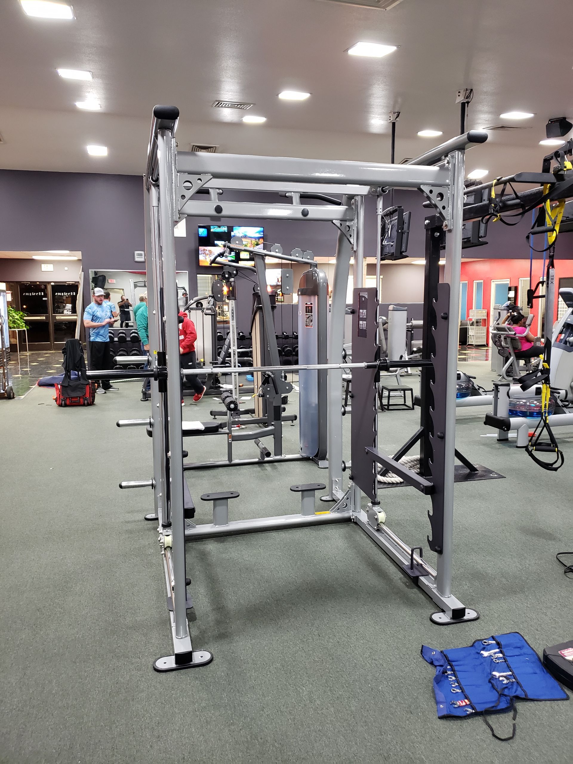 Gym interior with a cable machine in the foreground and exercise equipment scattered around.