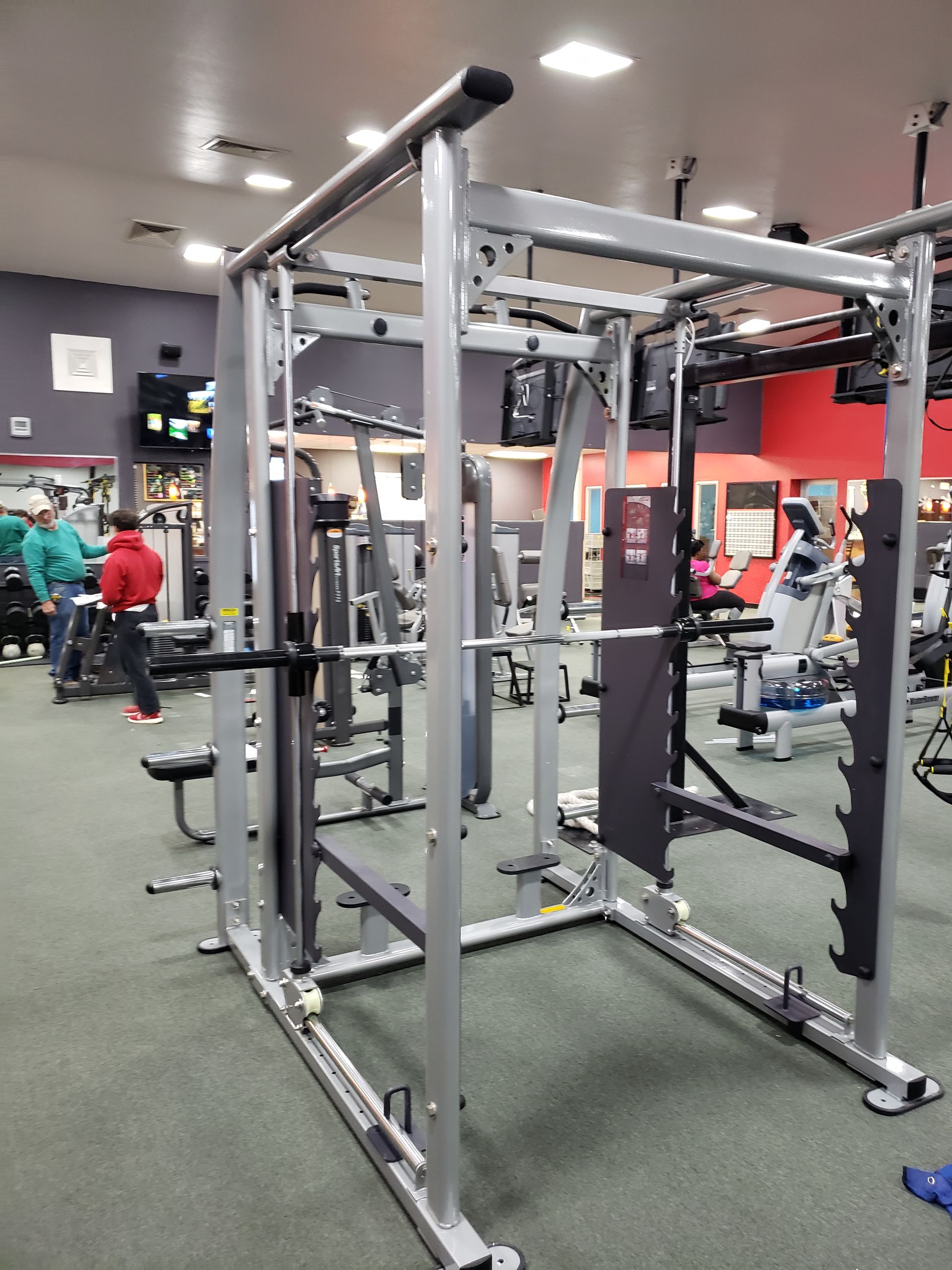 Gym cable machine in a fitness center, with gray metal frame and weight stacks in the background.