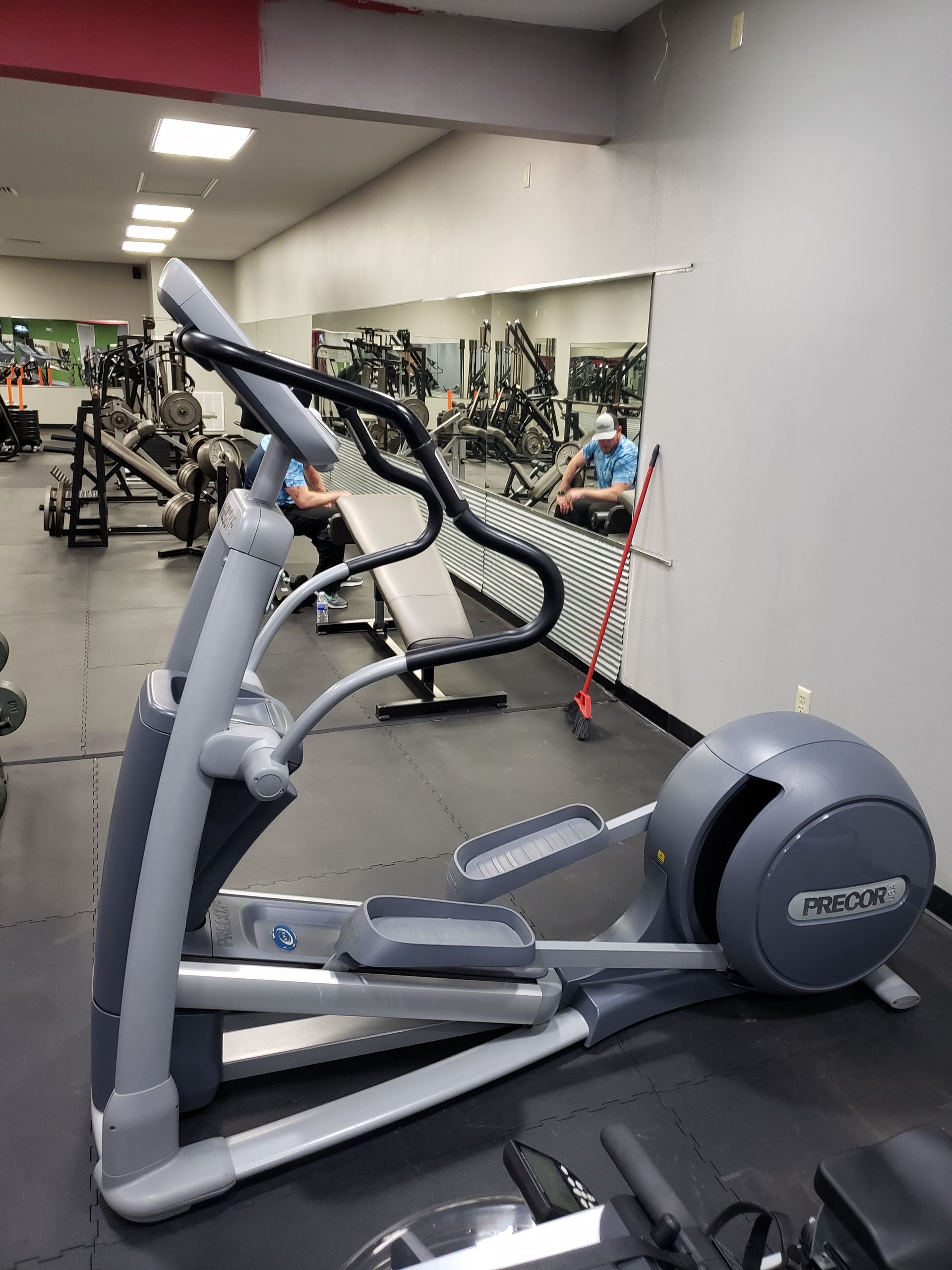 Elliptical machine in a gym with mirrored wall and workout equipment