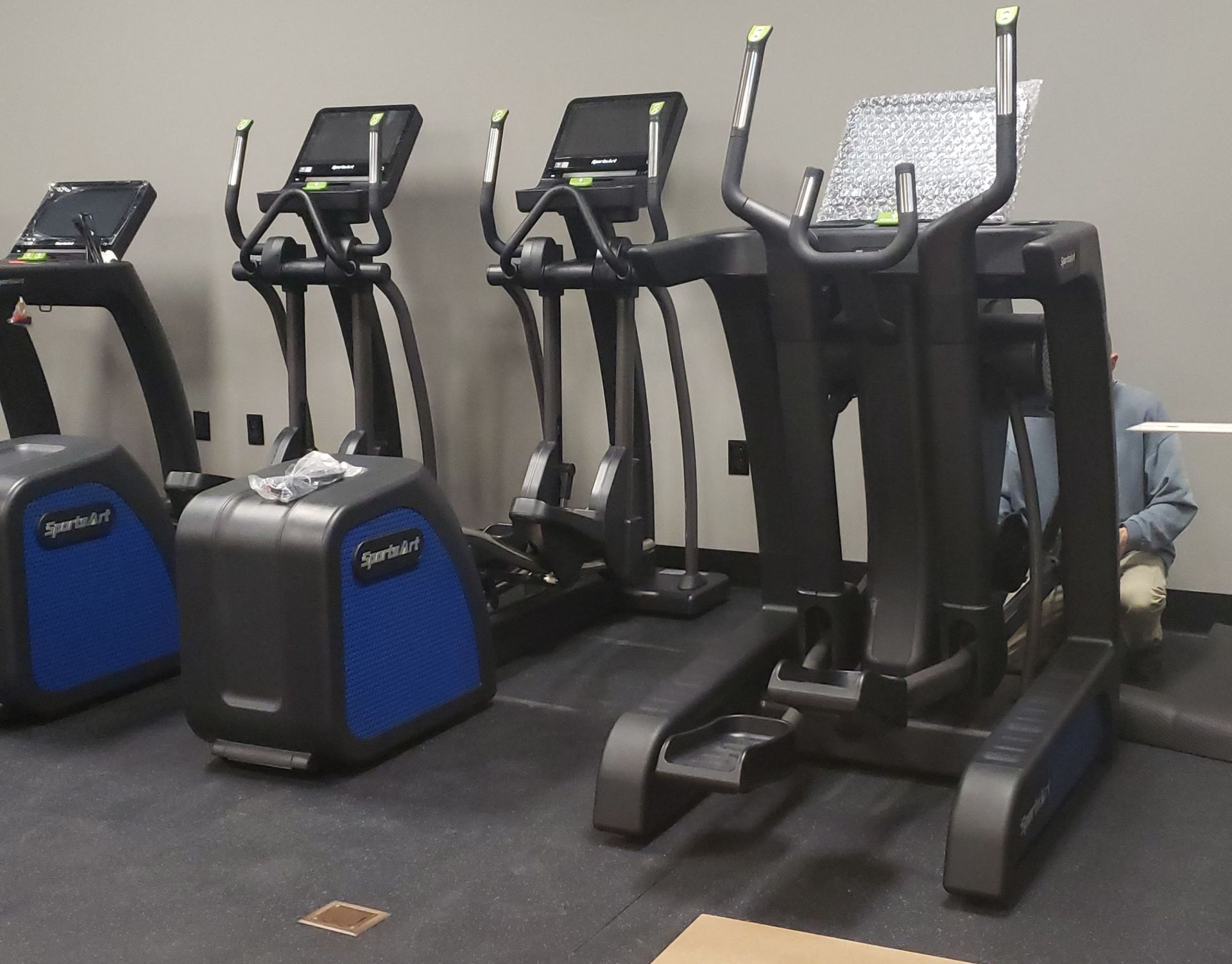 Several black and blue cardio machines lined up in a gym.