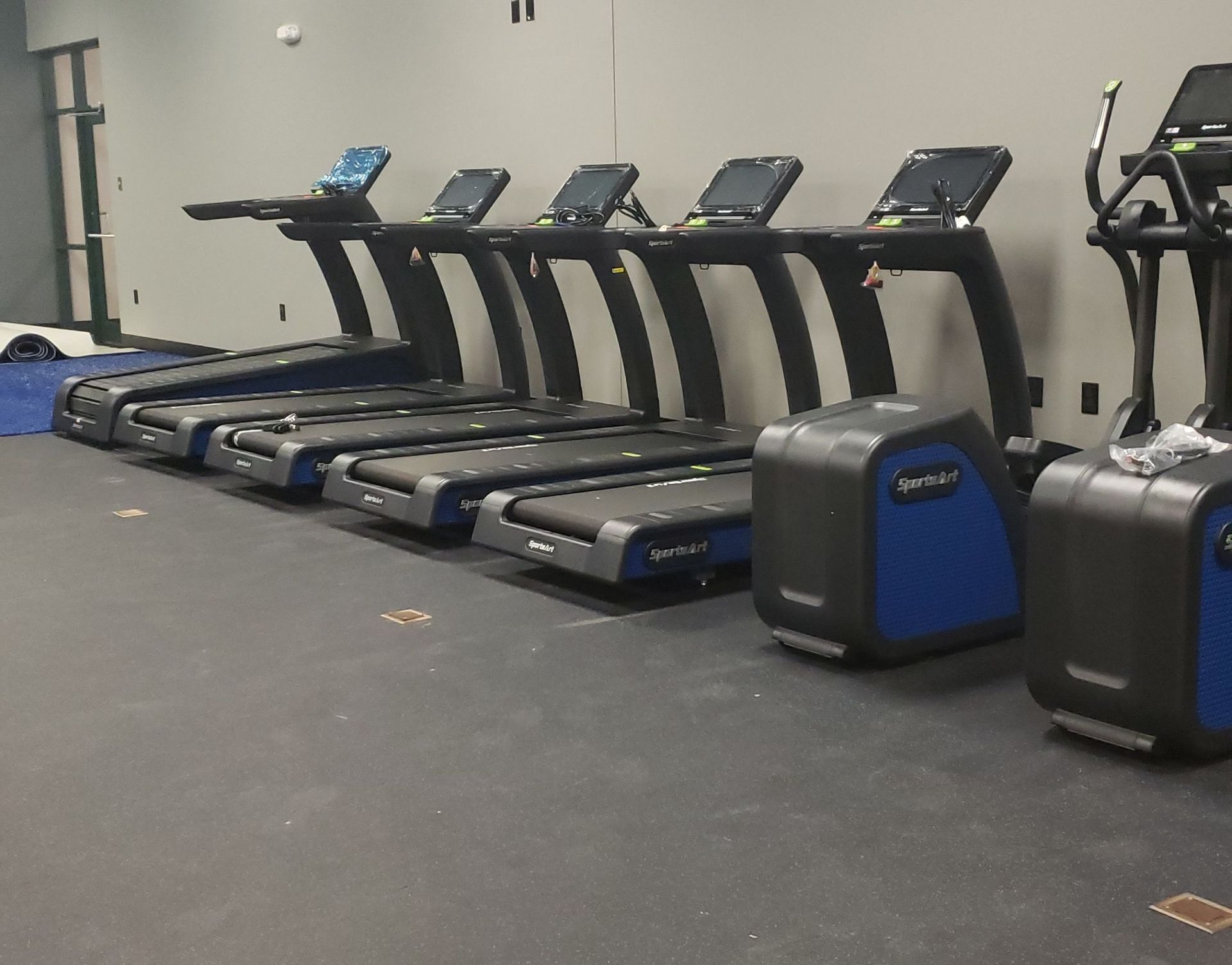 Row of treadmills in a gym, with gray floors and beige walls.