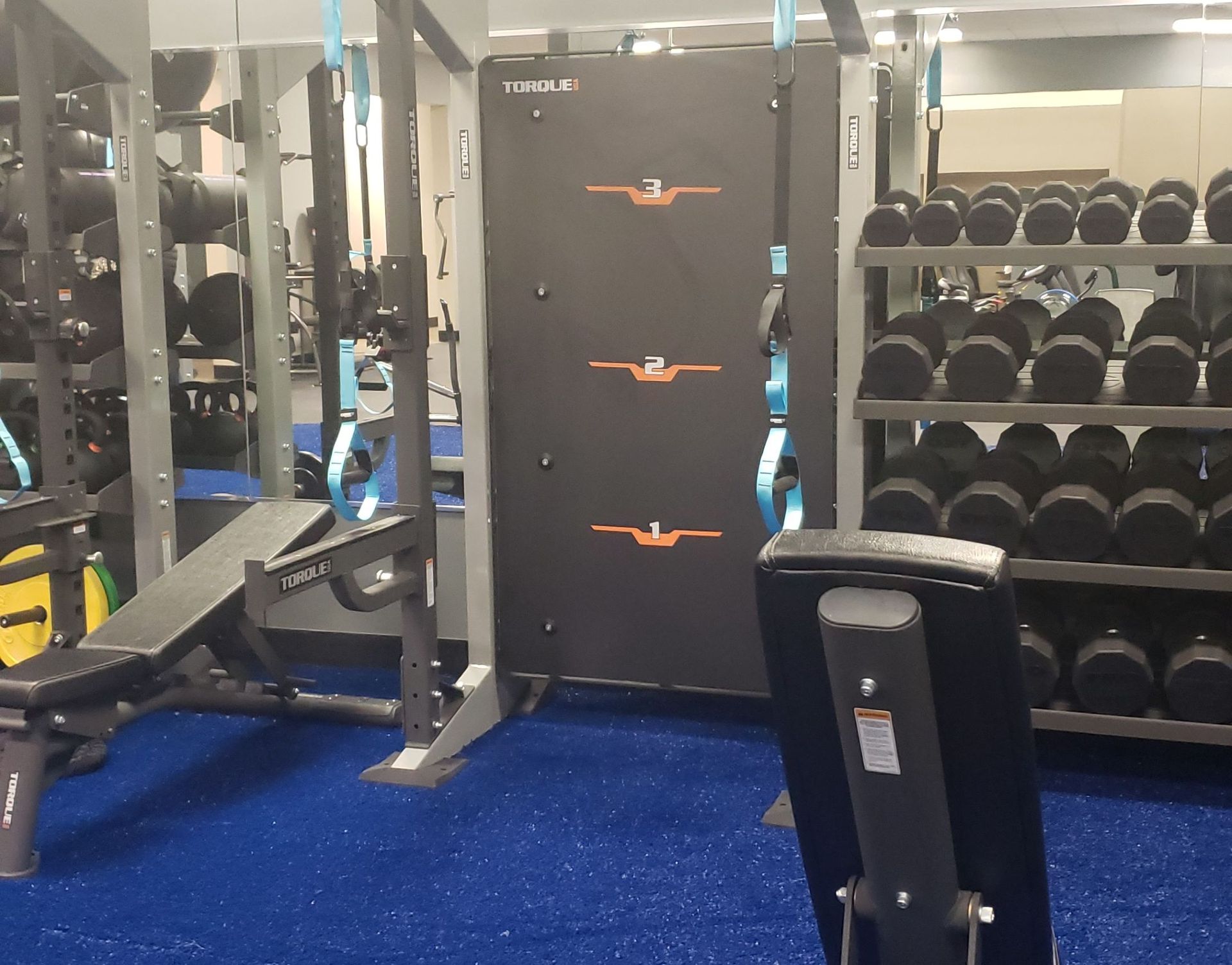 Gym weight room with cable machine, bench, and dumbbell rack on blue flooring