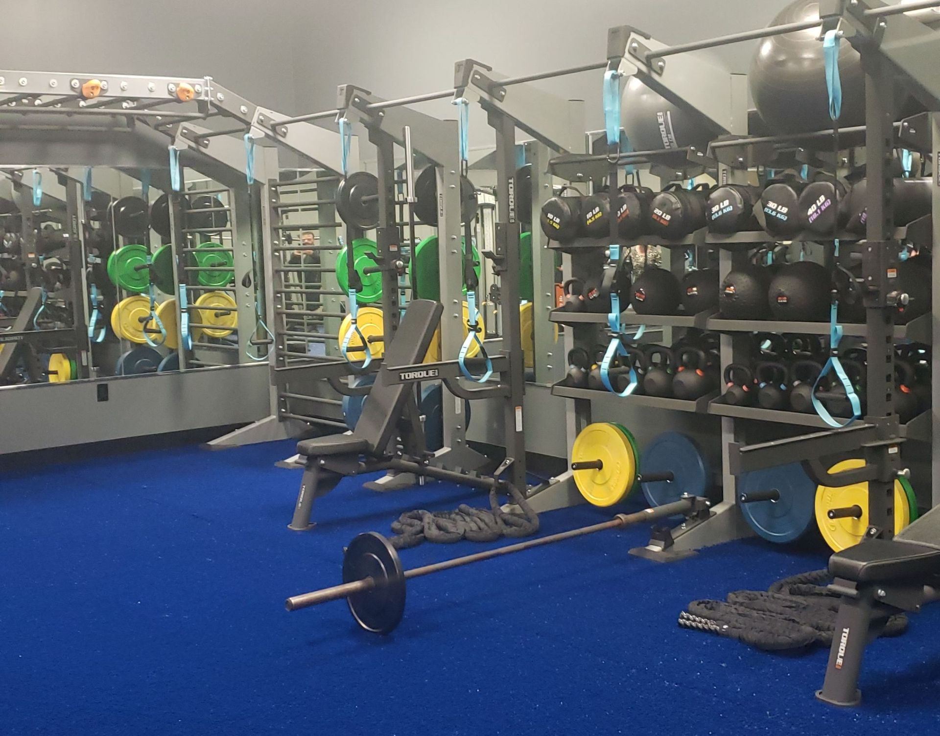 Gym with weight racks, barbells, exercise machines, and blue flooring.